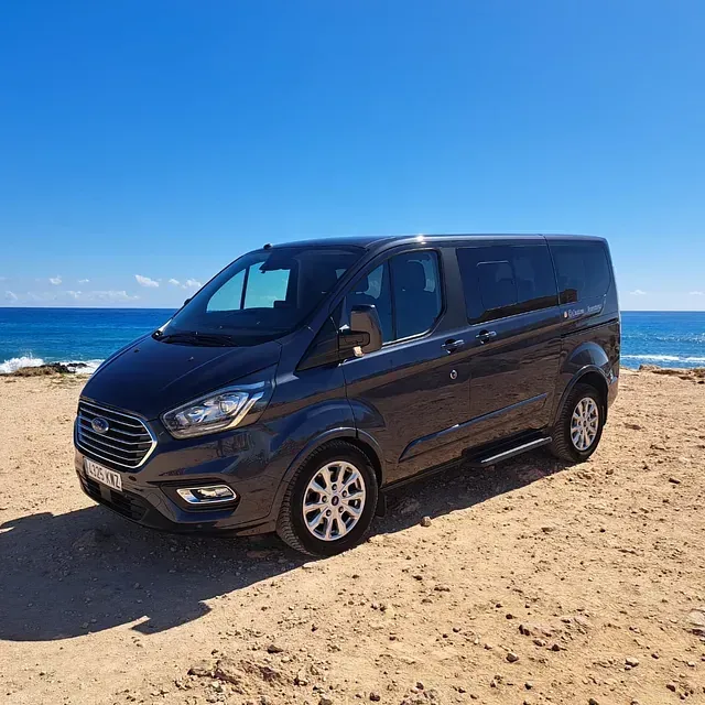 Una camioneta negra está estacionada en una playa de arena cerca del océano.