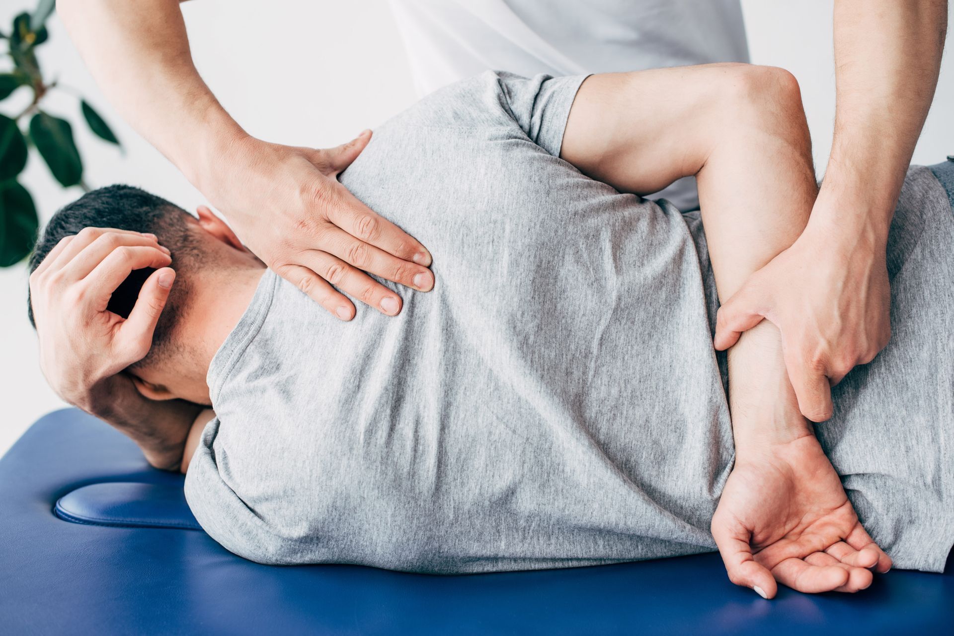 Une personne reçoit un massage du cou et du dos sur un tapis bleu, vêtue d'une chemise grise.