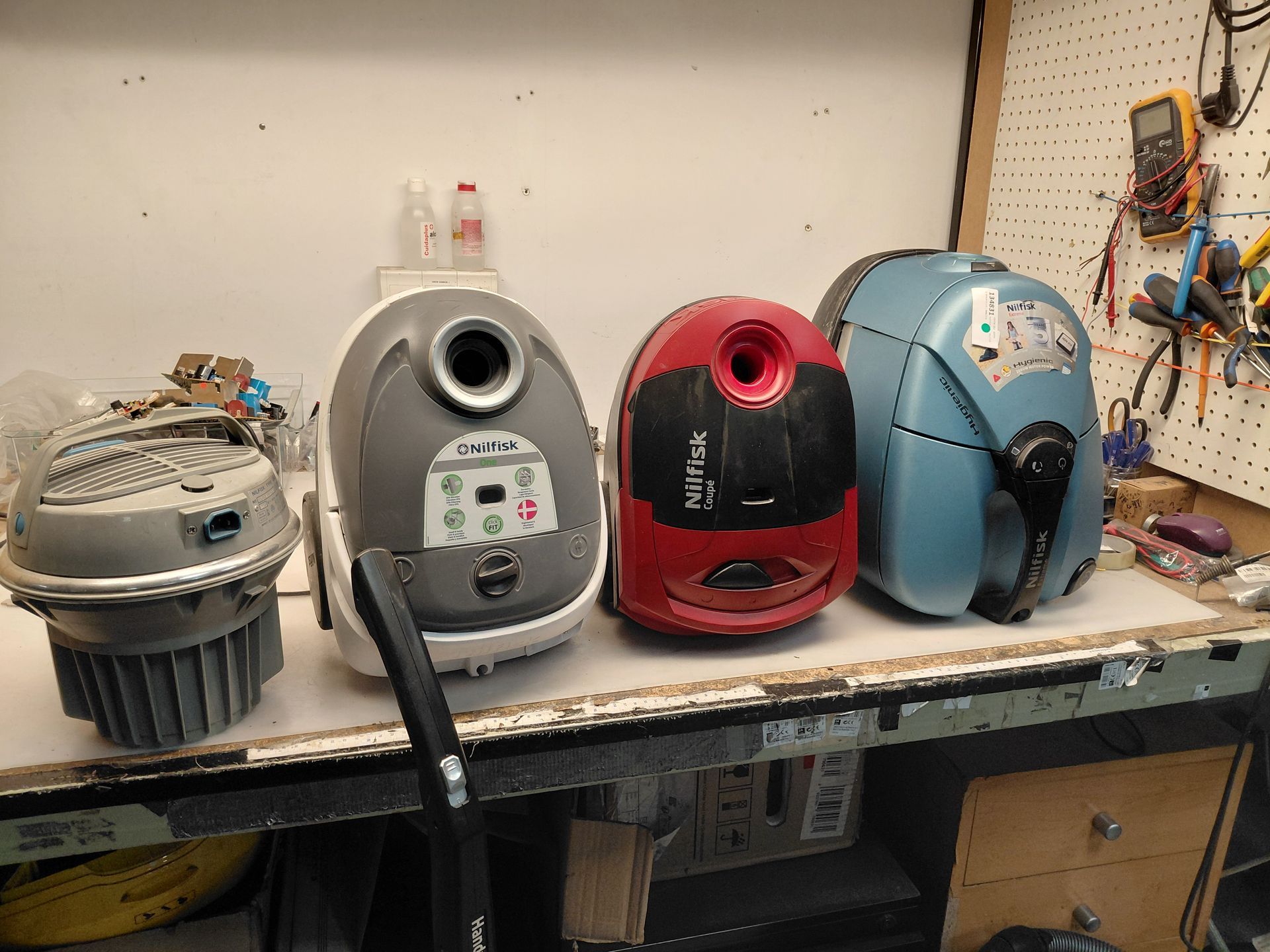 Las piezas de la lavadora, incluidas mangueras, motores, válvulas y módulos de control, están dispuestas sobre un fondo blanco.