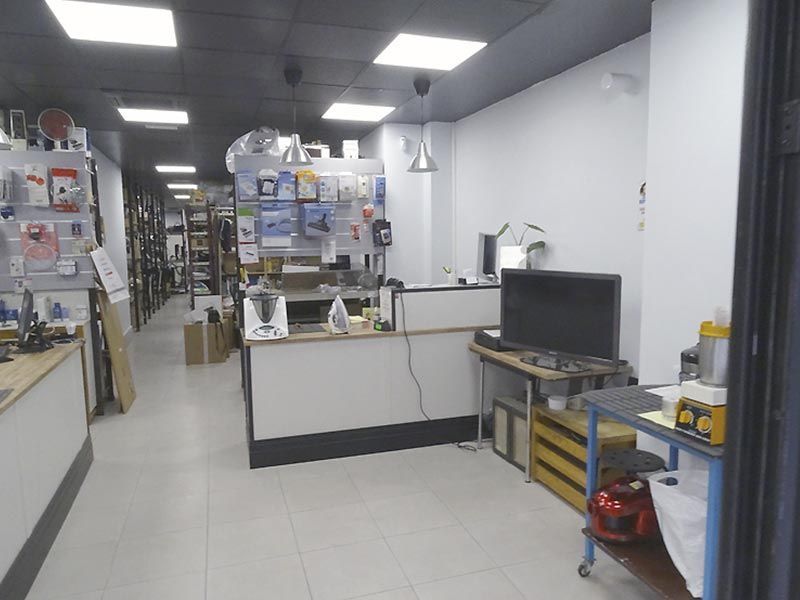 Interior de una tienda con estanterías, mostrador y aparatos electrónicos. Iluminación brillante y distribución sencilla.