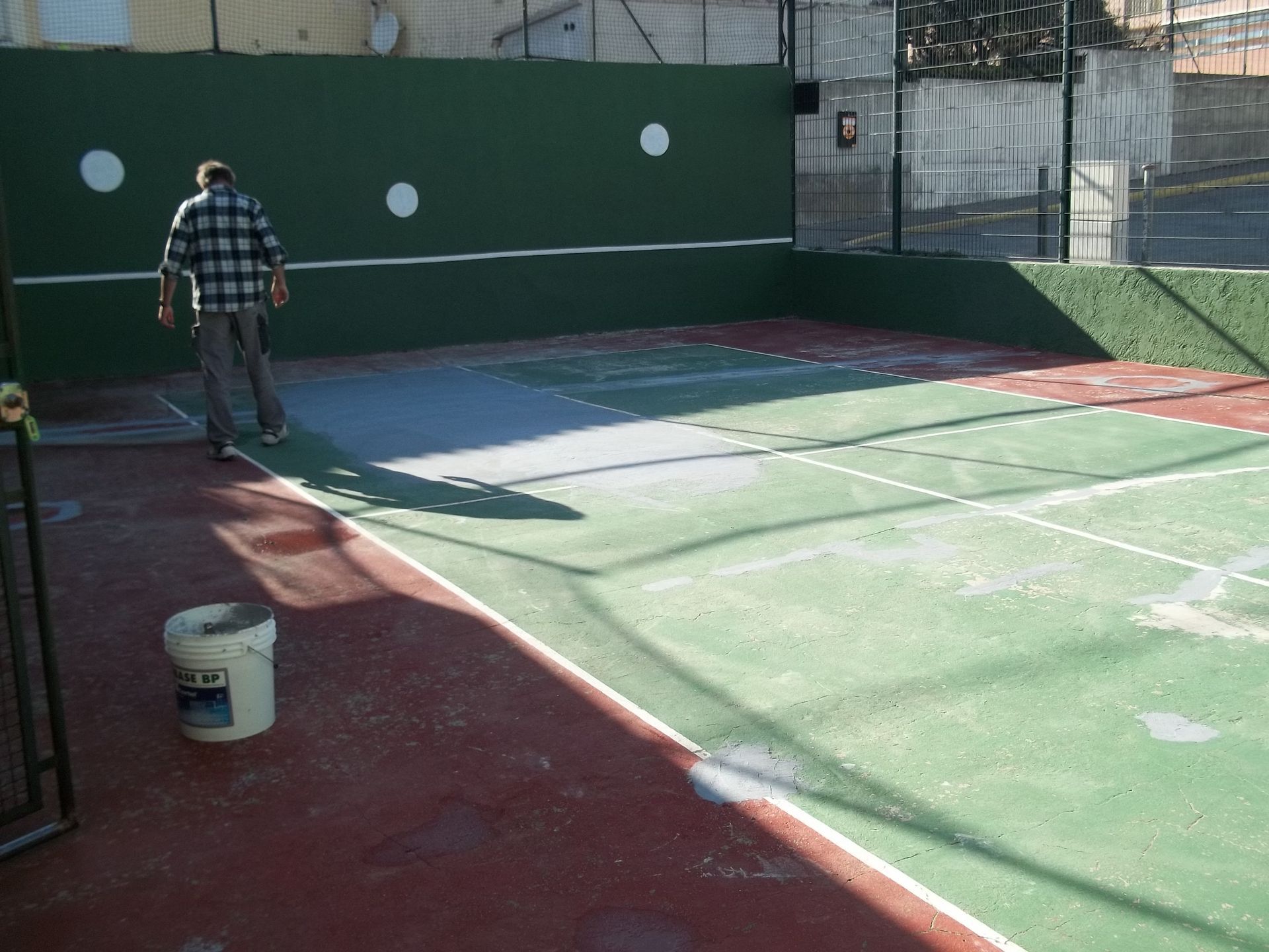 Un homme marche sur un terrain multicolore avec un mur vert et un seau de peinture.