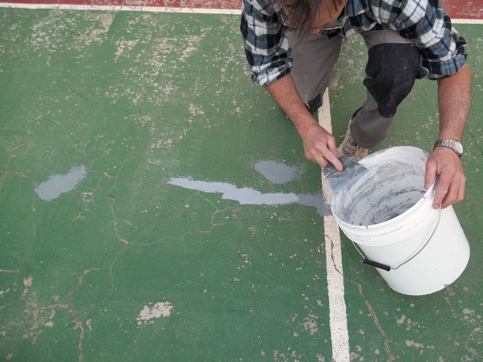 Une personne utilise une truelle pour appliquer un enduit gris provenant d'un seau blanc sur un terrain de sport vert.