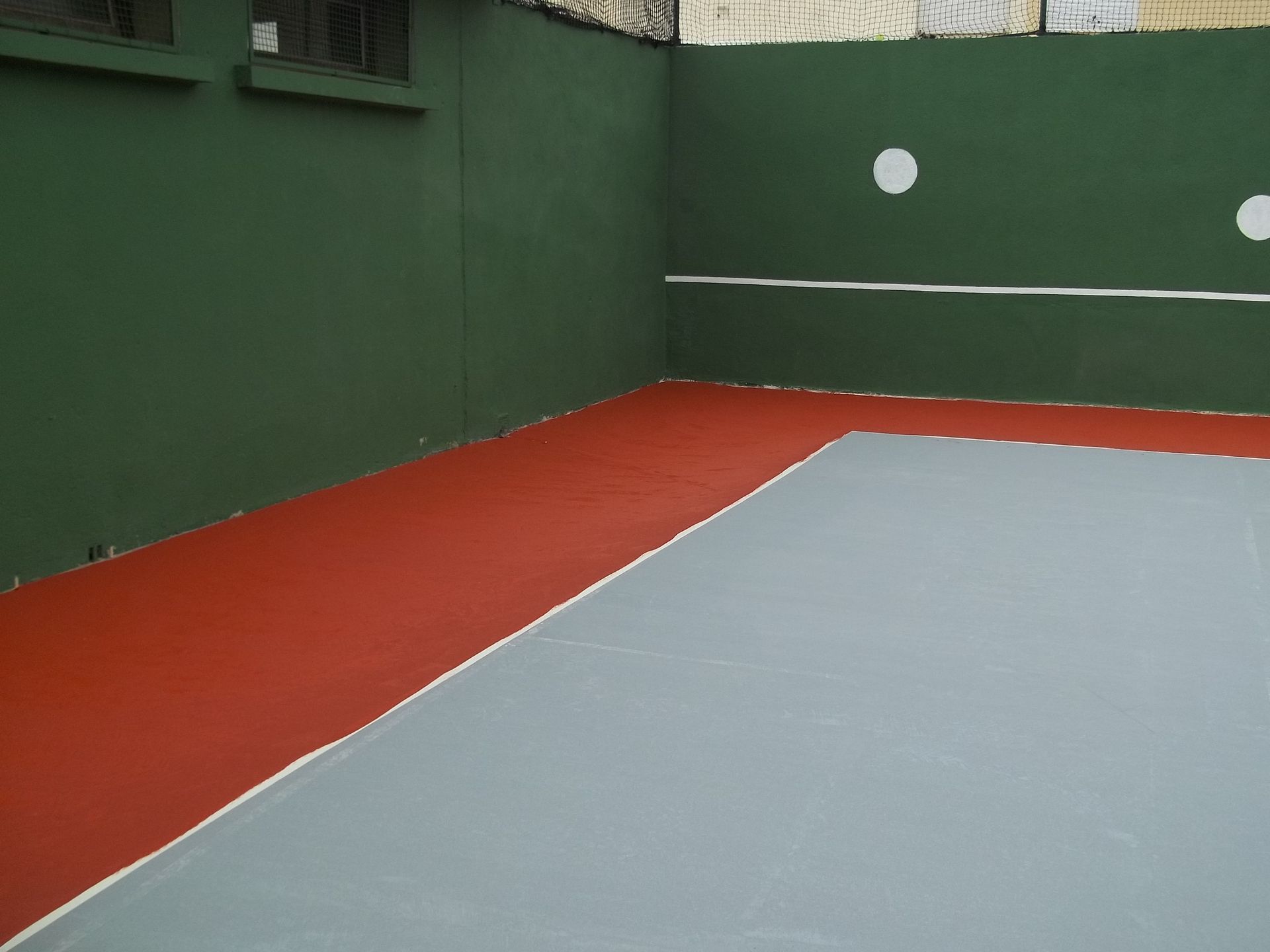 Un terrain de racquetball avec des murs verts, une ligne blanche et des sections de sol rouges et grises.