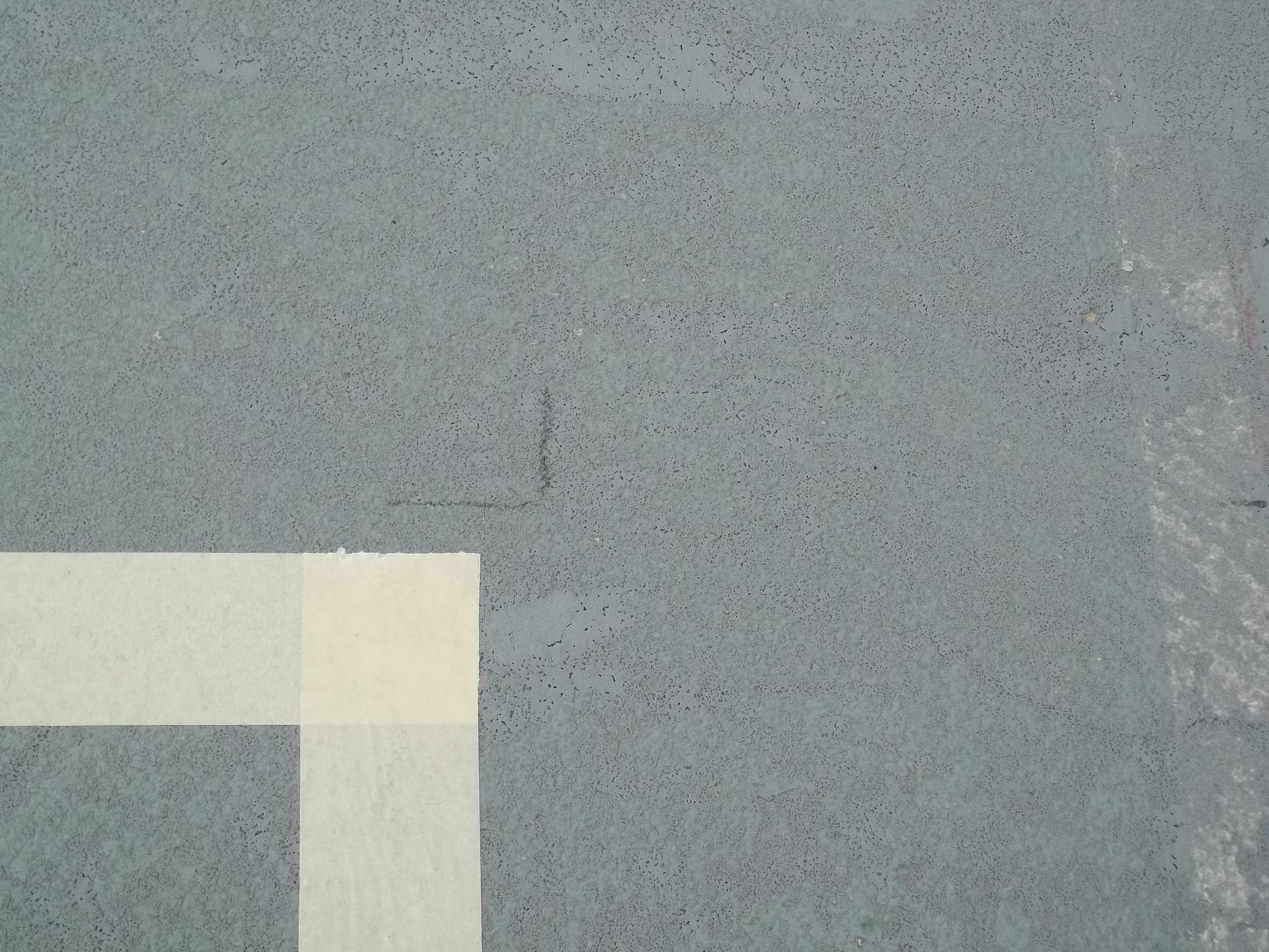 Surface texturée grise avec du ruban adhésif de masquage blanc formant un angle.
