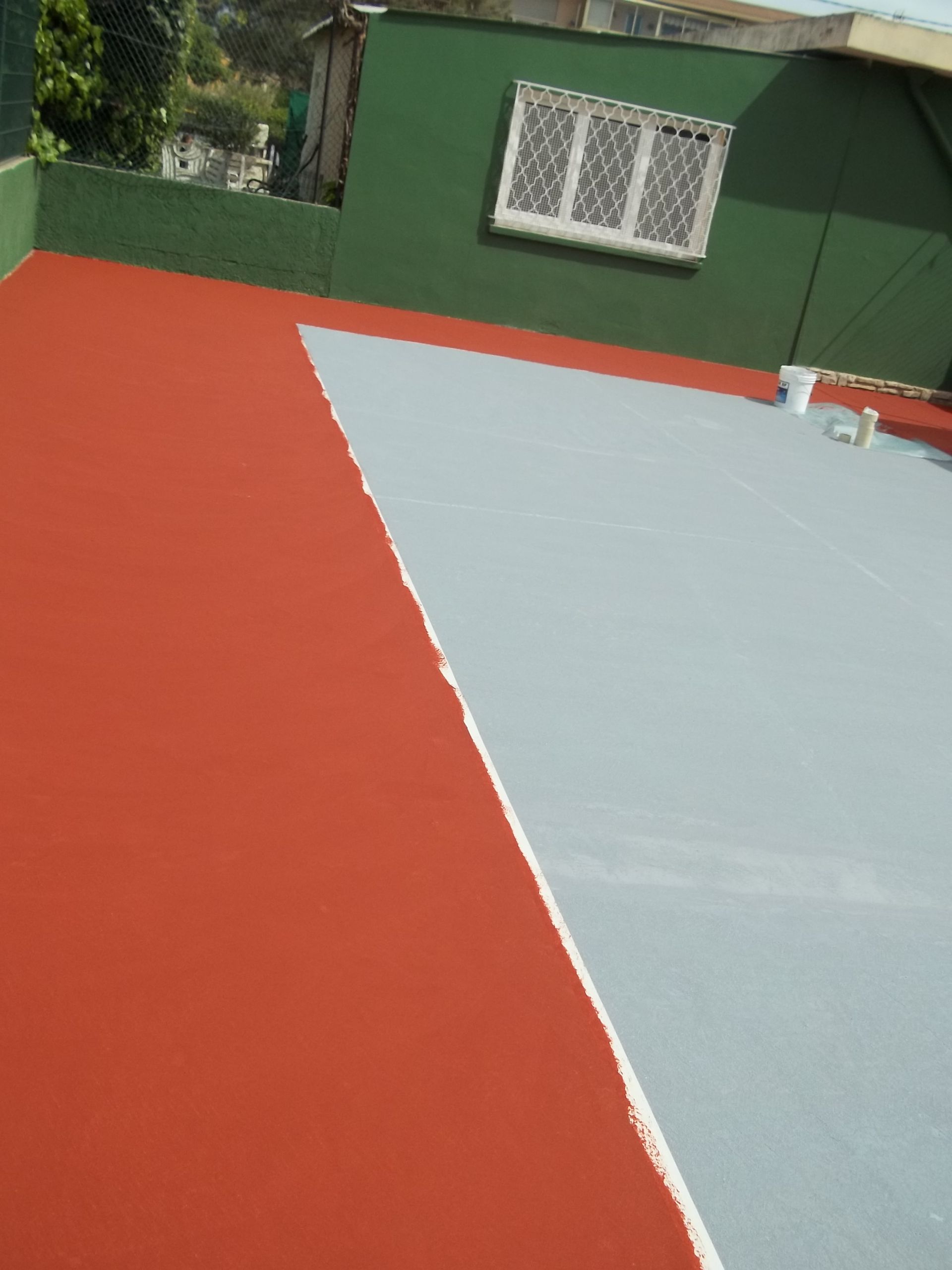 Toit peint en rouge et gris, mur vert avec fenêtre et un seau de peinture.