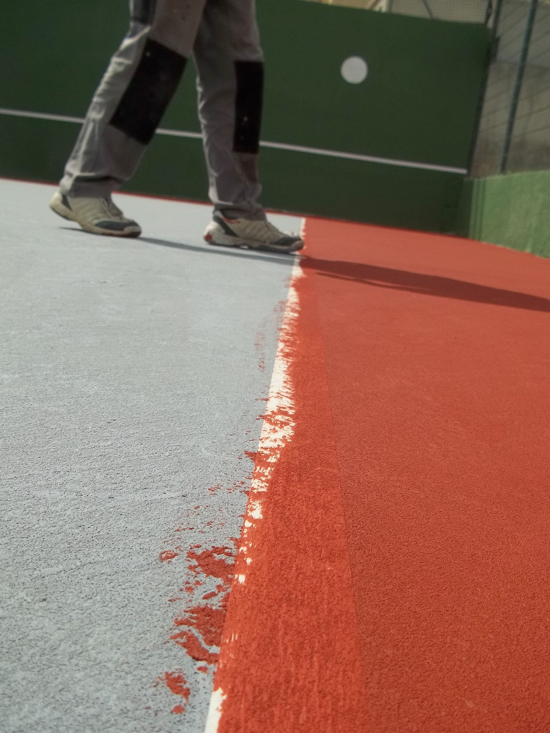 Une personne peint la surface d'un terrain de sport, la faisant passer du gris au rouge.