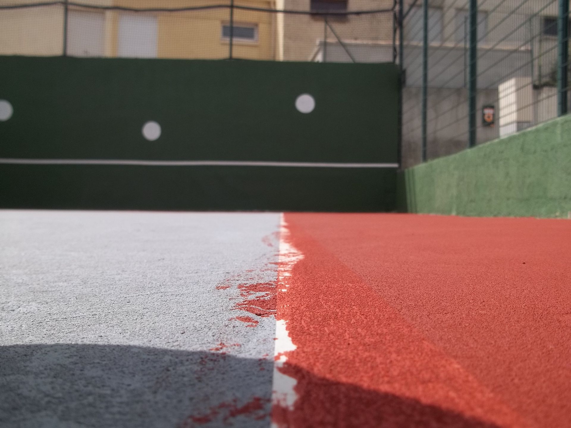 Gros plan sur un court de tennis montrant les surfaces peintes en rouge et en blanc, séparées par une ligne blanche.