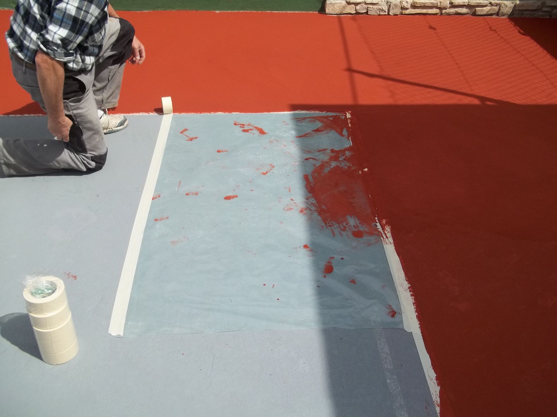 Une personne peint une surface grise en rouge ; du ruban adhésif blanc marque la limite. Les surfaces rouge et grise sont visibles.