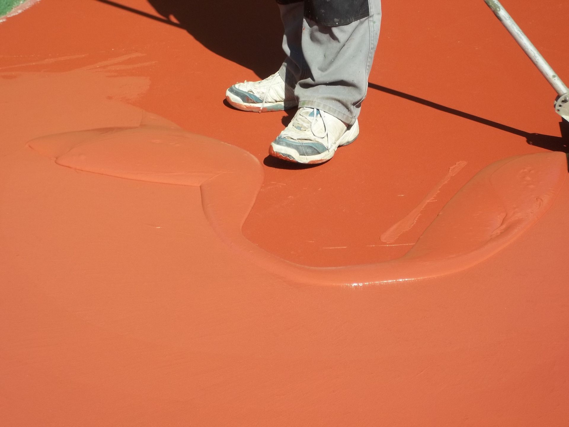 Une personne applique un revêtement rouge sur une surface à l'aide d'un rouleau, en extérieur.