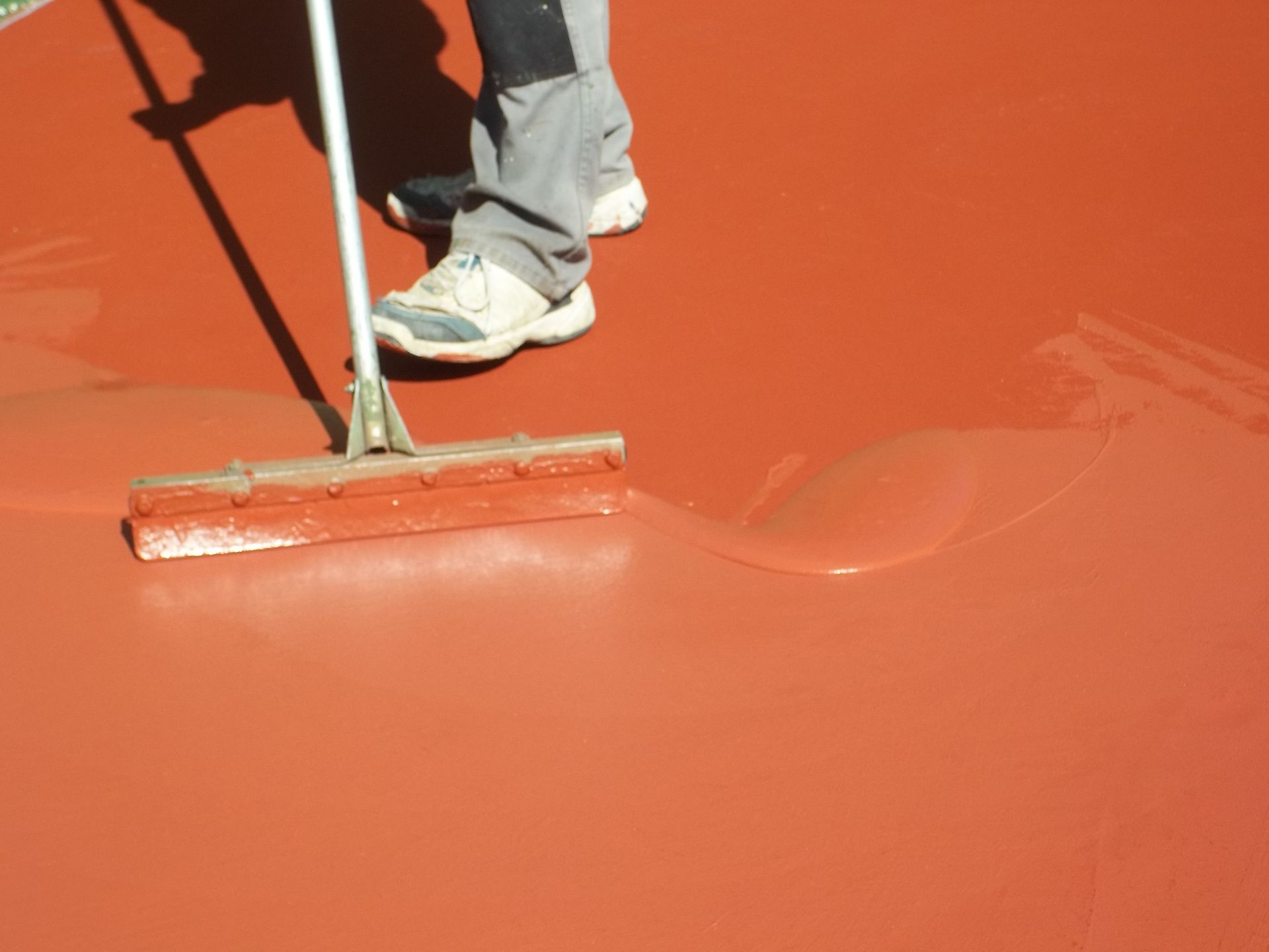 Personne utilisant une raclette pour étaler du mastic orange sur une surface.