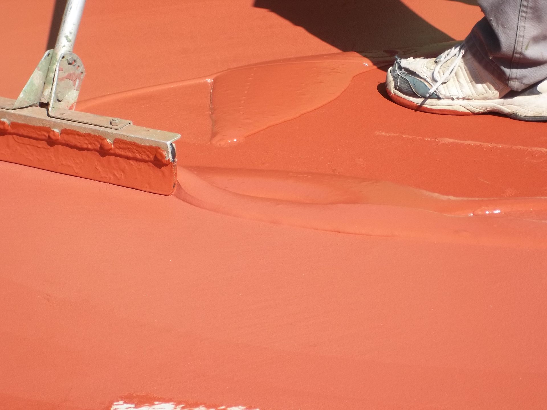 Personne appliquant un revêtement orange sur une surface à l'aide d'une raclette.
