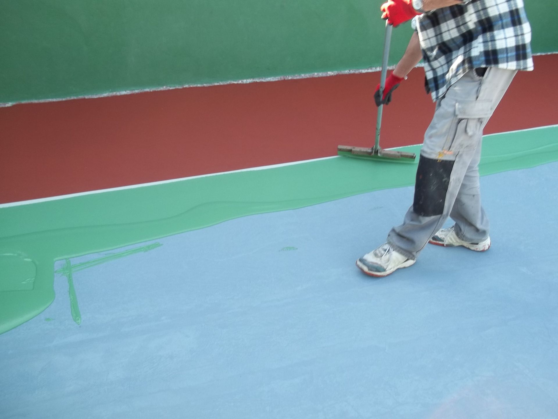 Personne appliquant un revêtement bleu sur la surface d'un court de tennis à l'aide d'un rouleau.