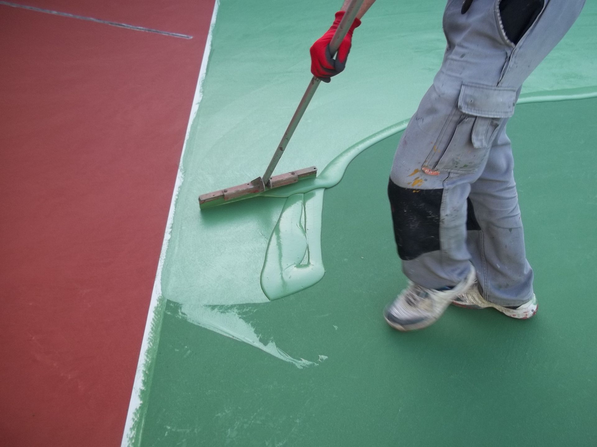 Une personne applique un revêtement vert sur une surface à l'aide d'une raclette ; des zones rouges et vertes sont visibles.