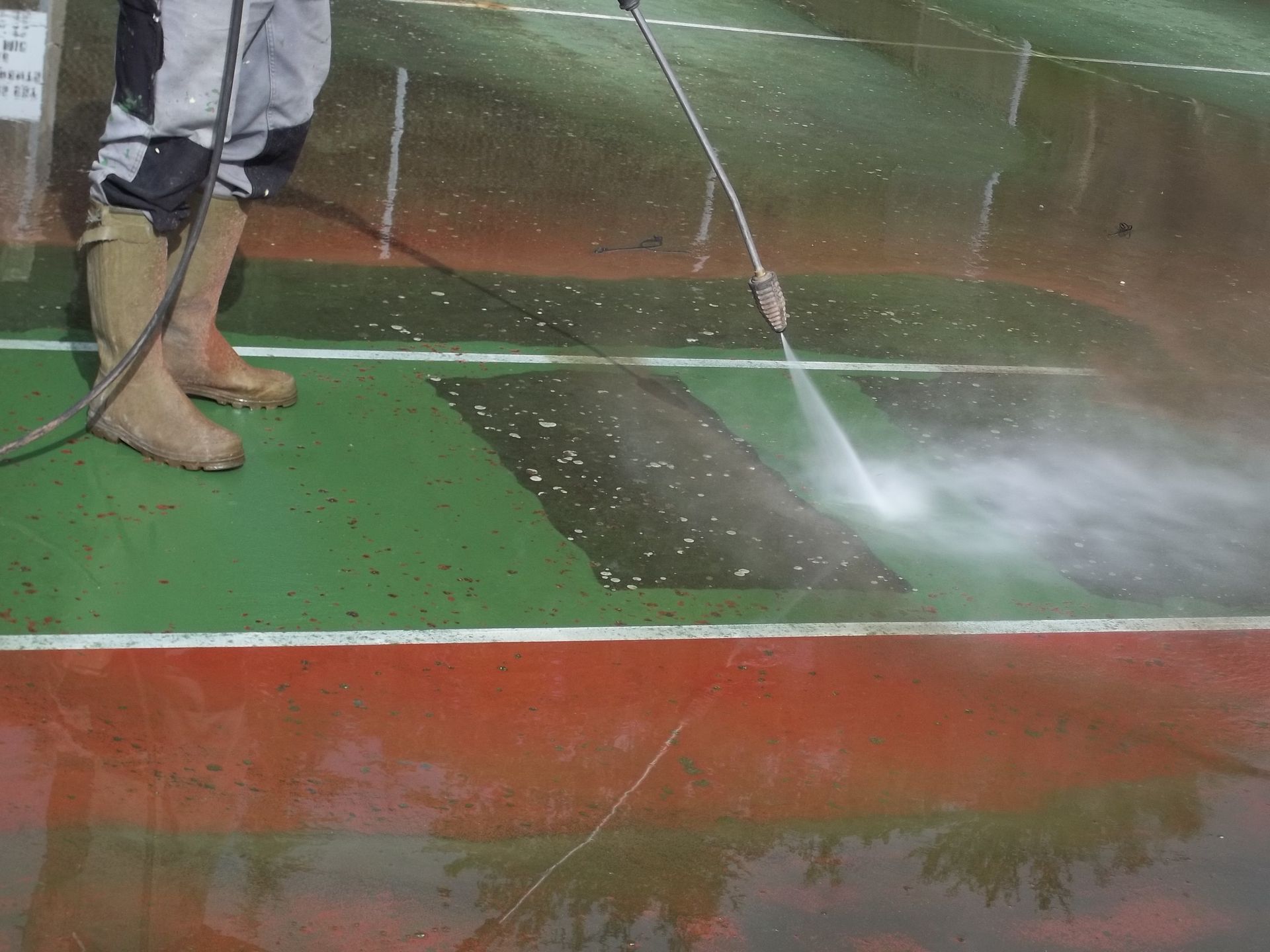Une personne portant des bottes nettoie à haute pression un terrain de sport multicolore.