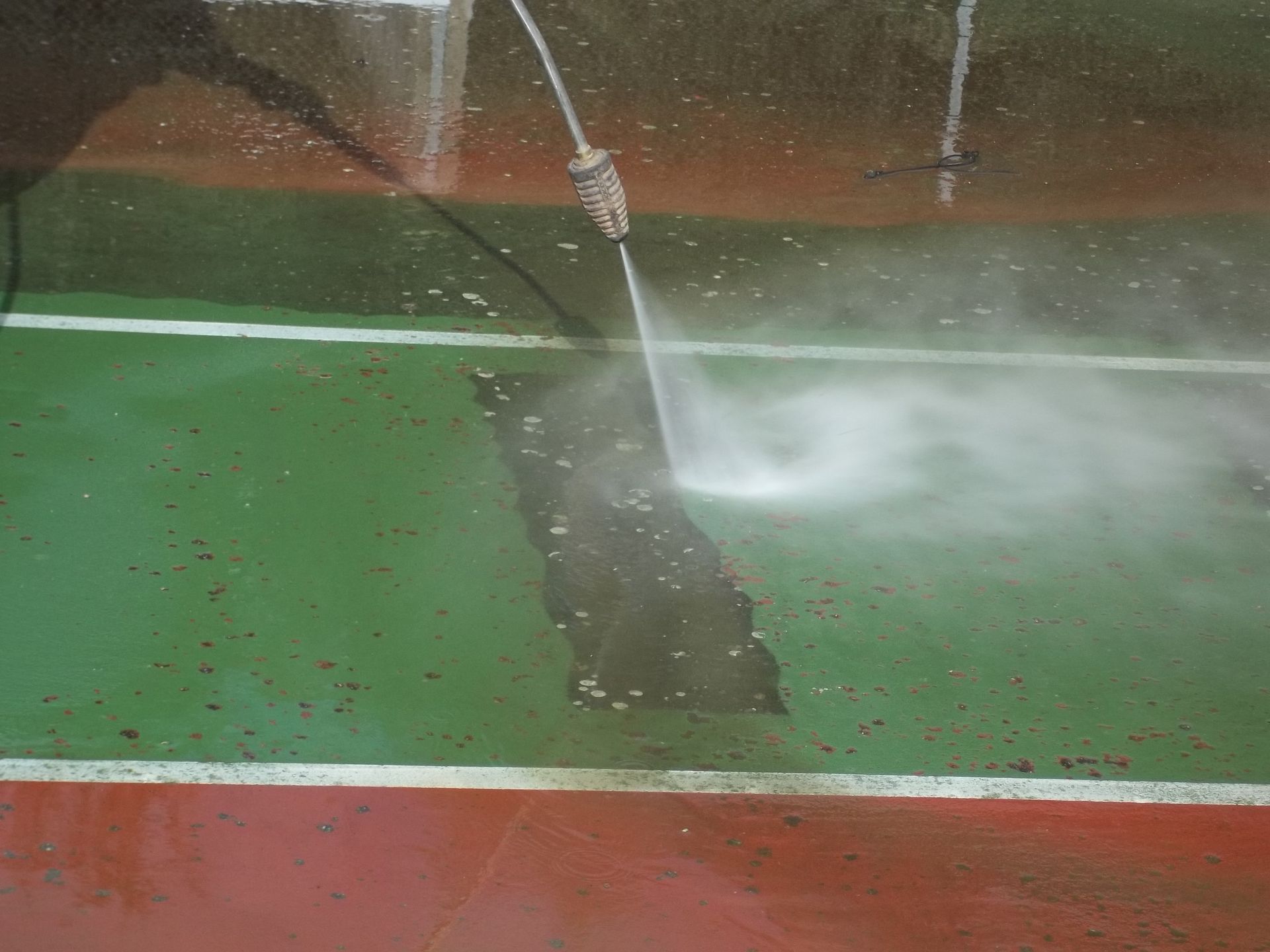 Nettoyage à haute pression d'un court de tennis peint en vert et rouge, pour effacer les lignes blanches.
