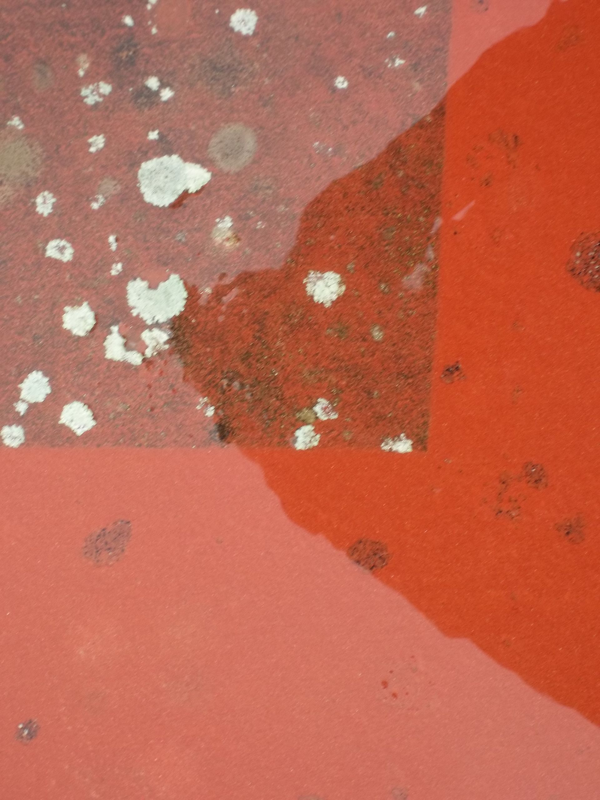 Œuvre abstraite rouge patinée, avec des zones plus claires et plus foncées et des taches de décoloration.