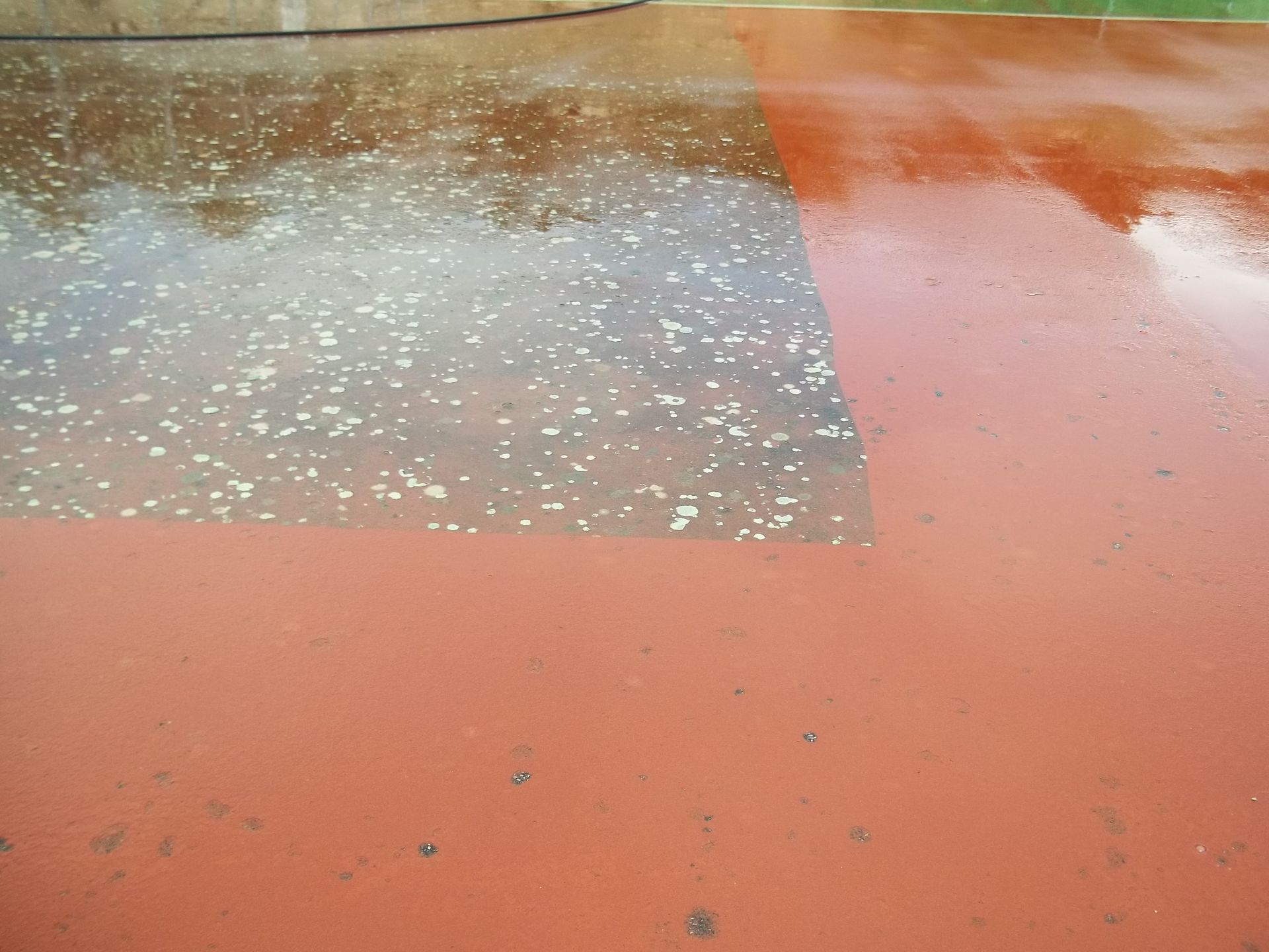 Surface peinte en rouge et gris partiellement nettoyée à l'eau.