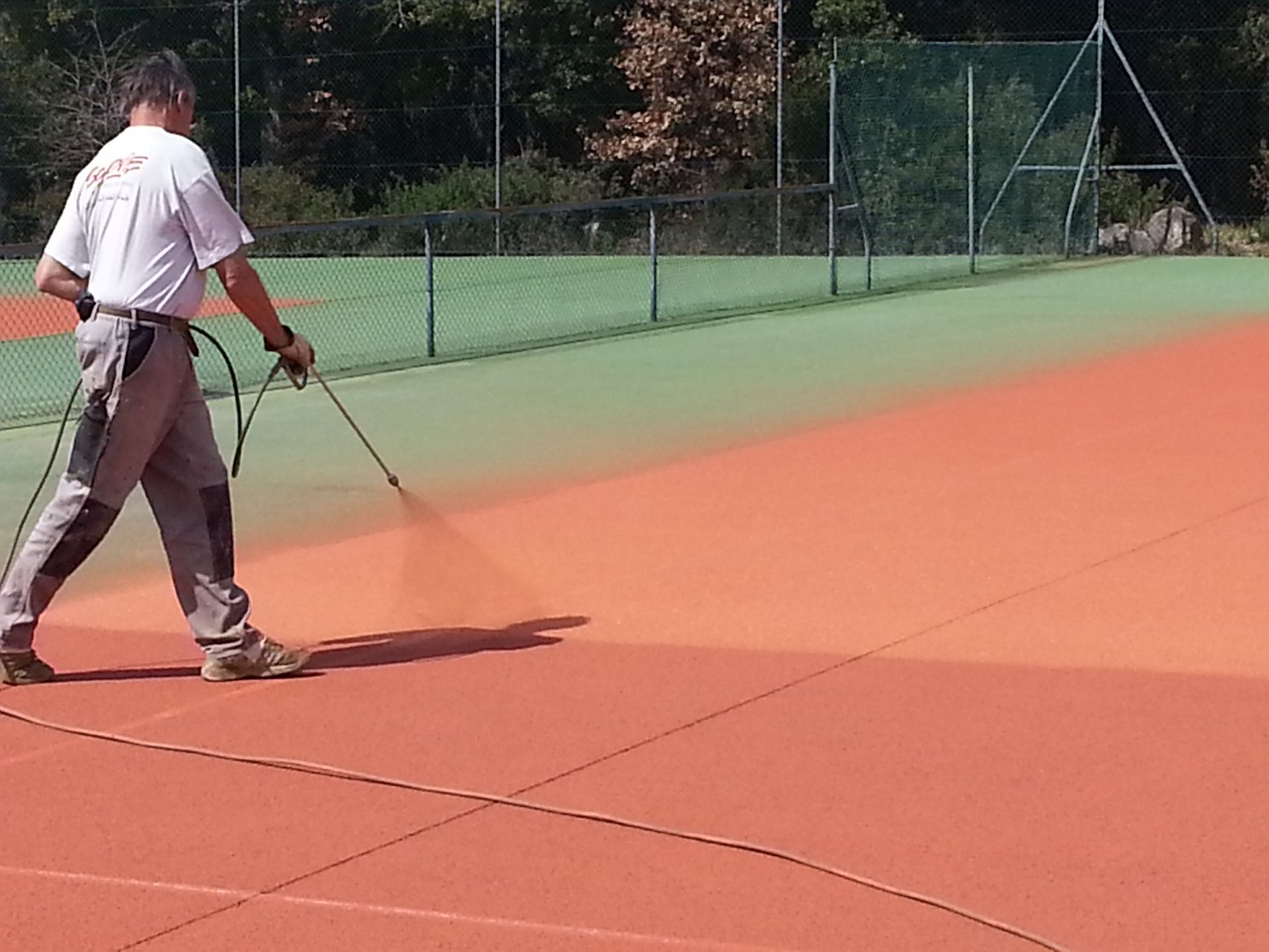 Un homme vaporise de la peinture sur un court de tennis, passant du vert au rouge.