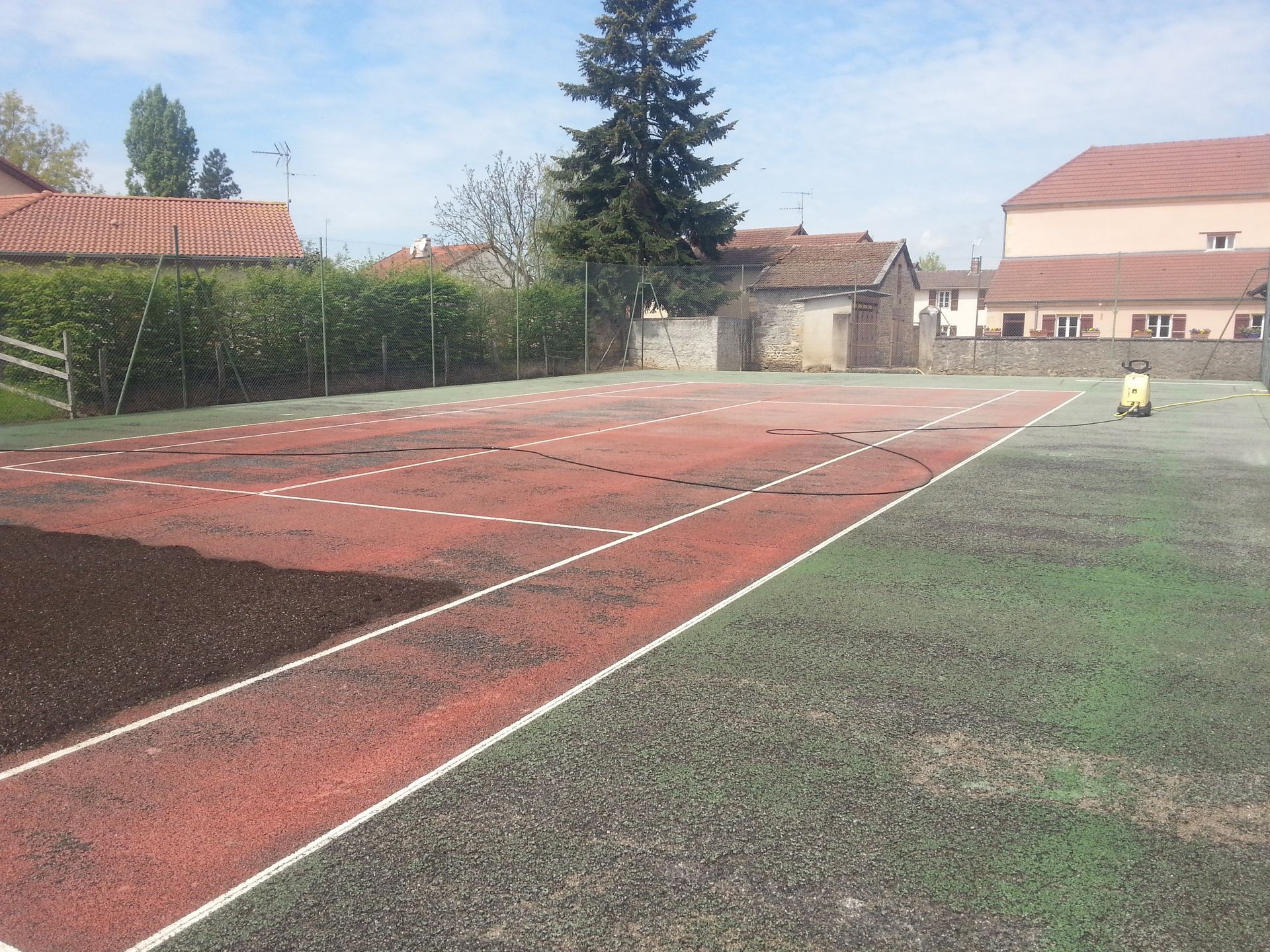 Terrain de sport extérieur avec surfaces rouges et vertes, lignes pointillées et bâtiments en arrière-plan.