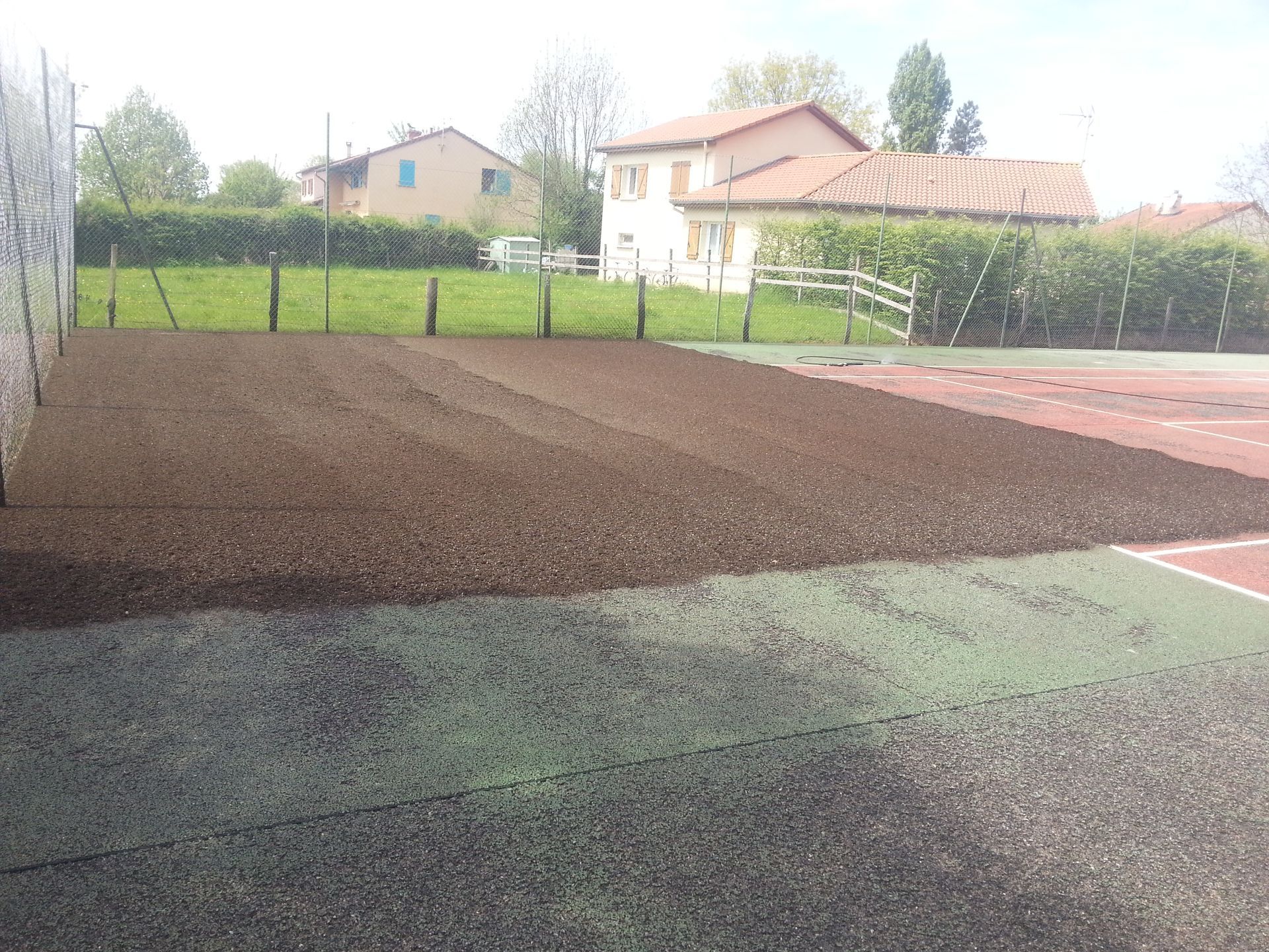 Lit de terre préparé à côté d'une cour multicolore, avec des maisons et de la verdure en arrière-plan.