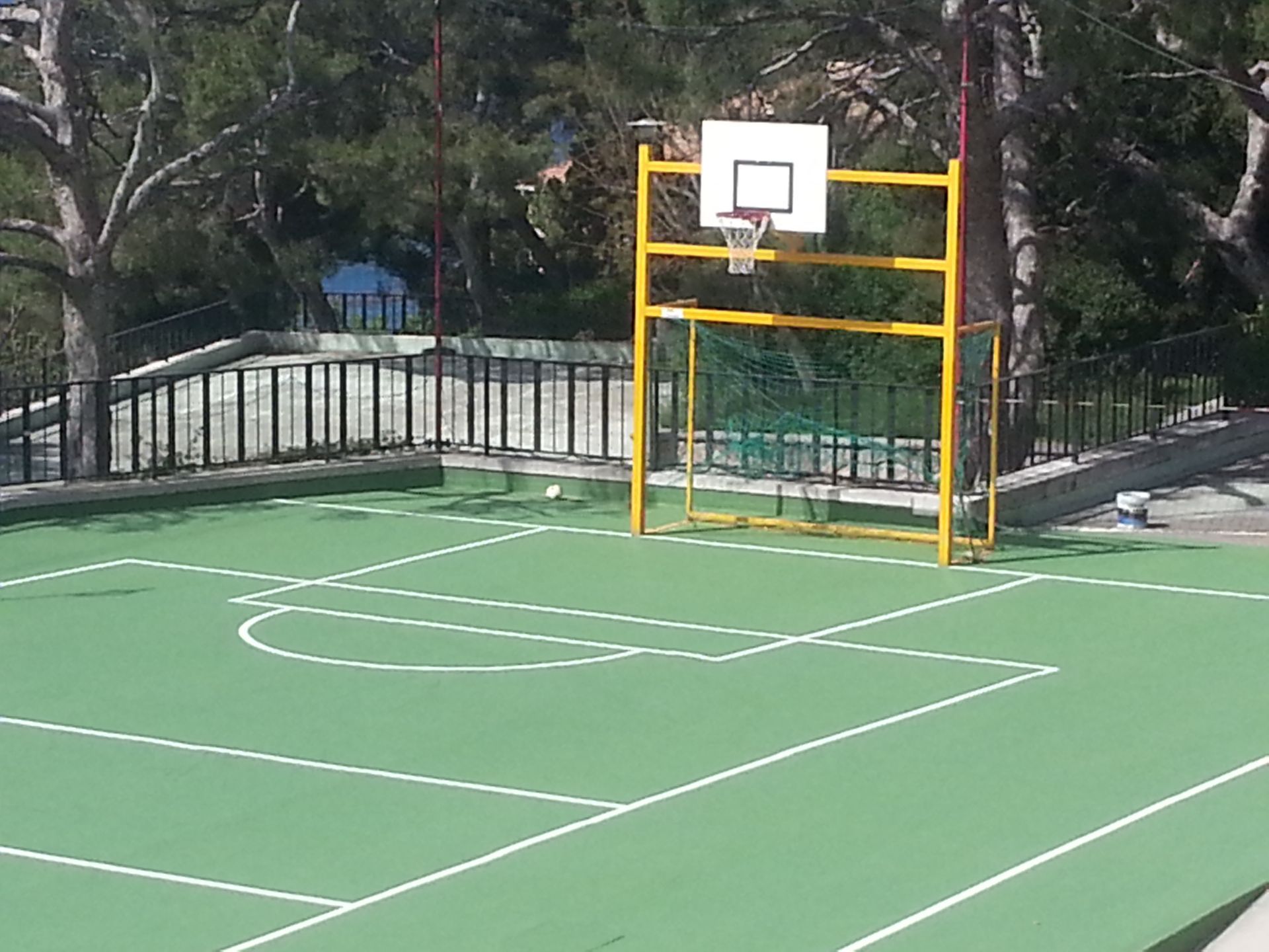 Terrain de basket avec surface verte, lignes blanches et panneau arrière jaune.