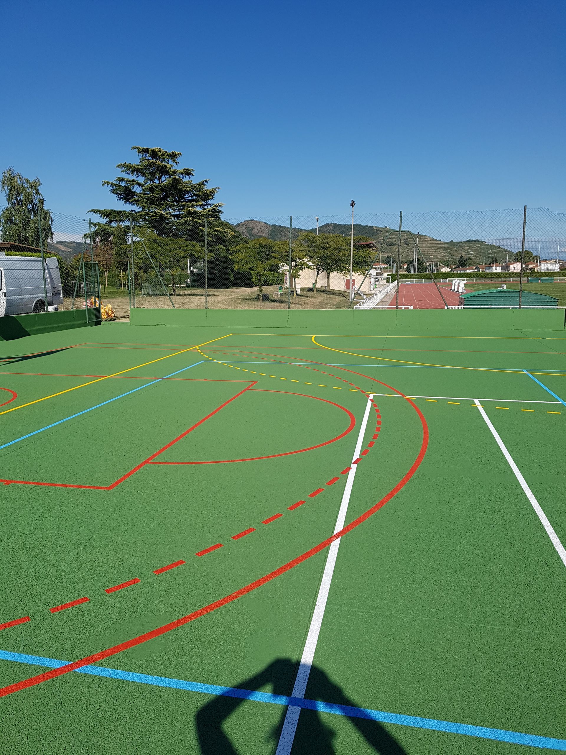 Terrain de gazon vert avec des lignes colorées pour le sport, sous un ciel bleu, ombre d'une personne.