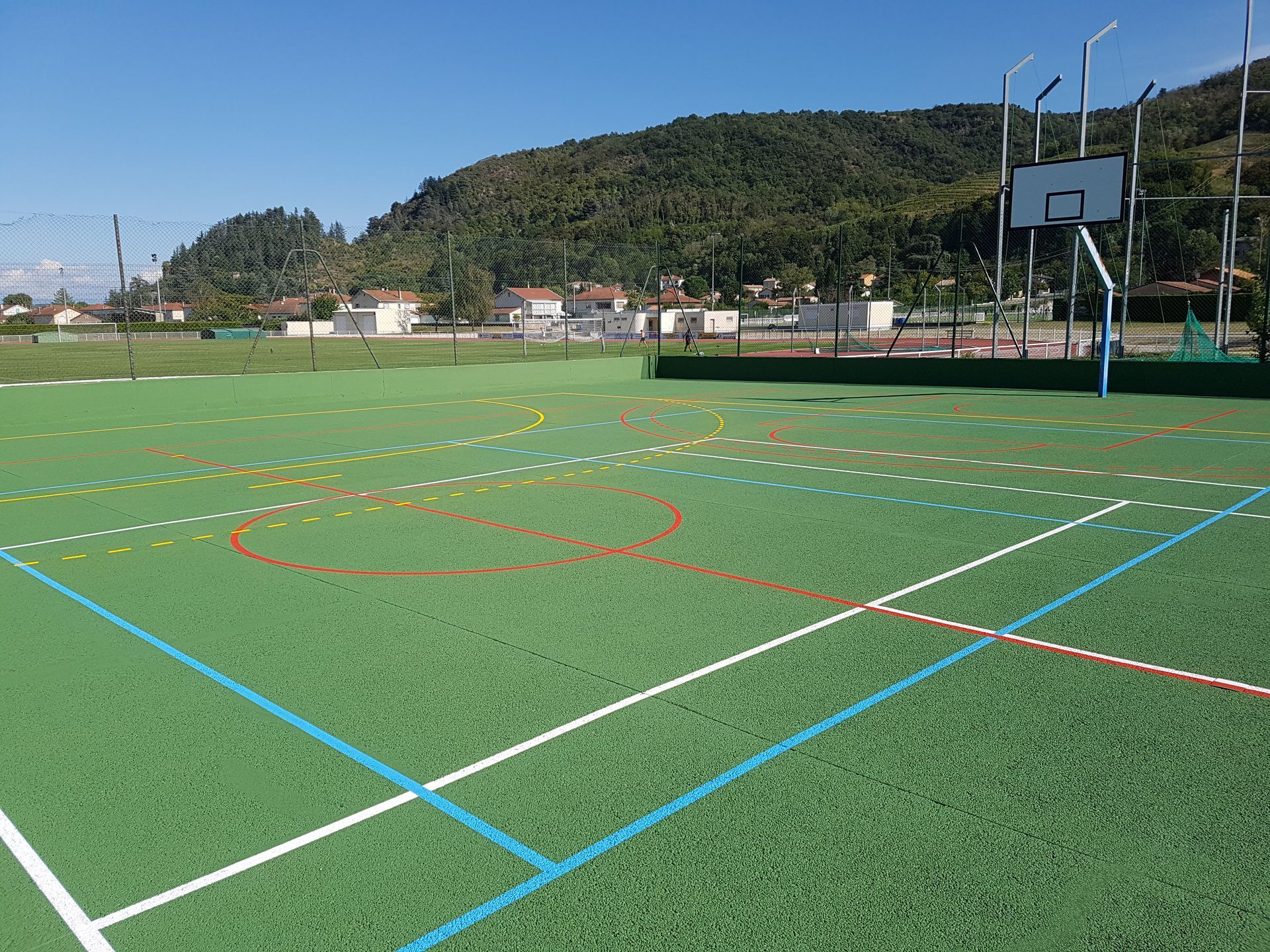 Terrain de sport vert avec lignes peintes et panier de basket, montagnes en arrière-plan.