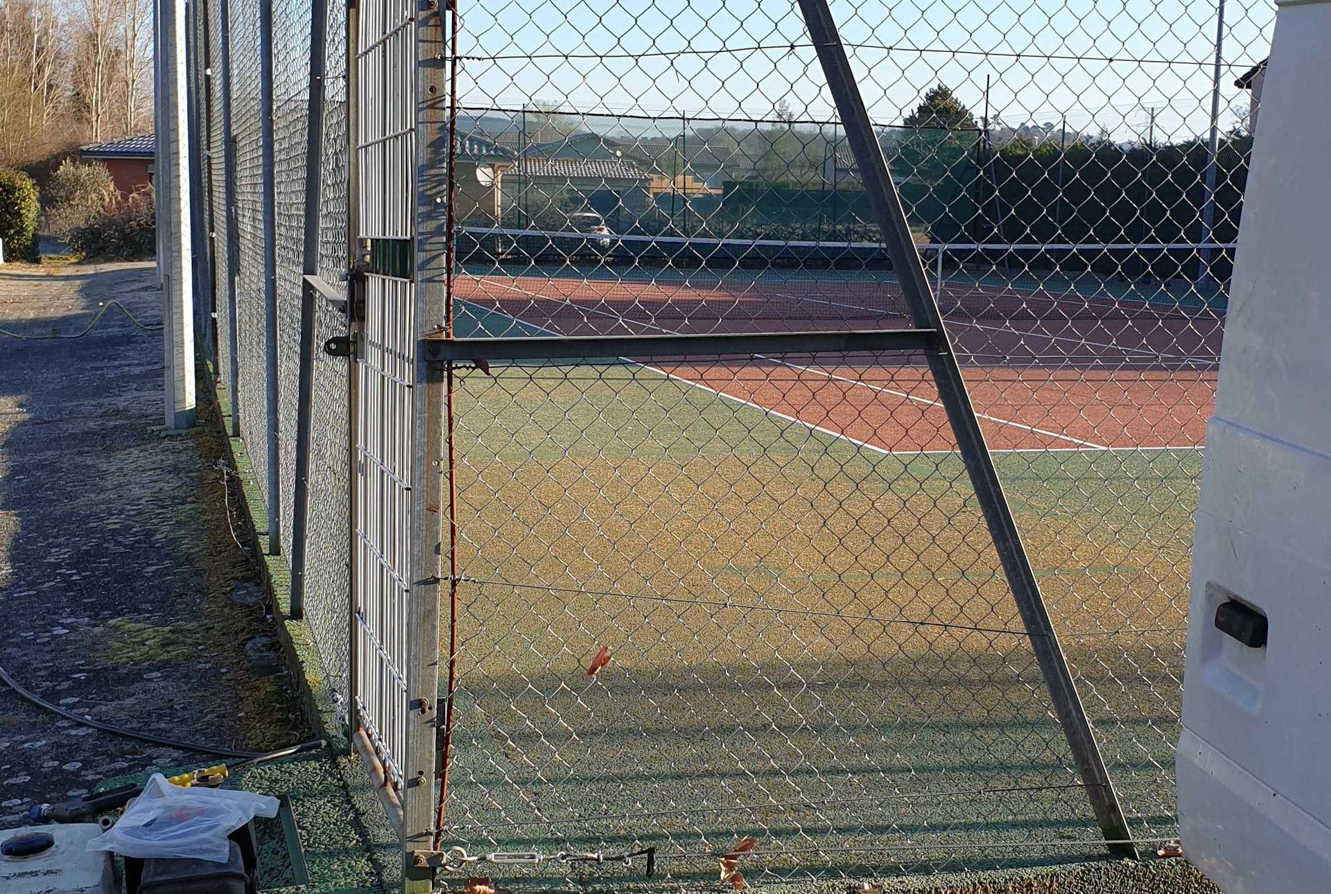Court de tennis vu à travers un grillage. Court vert et rouge, journée ensoleillée.