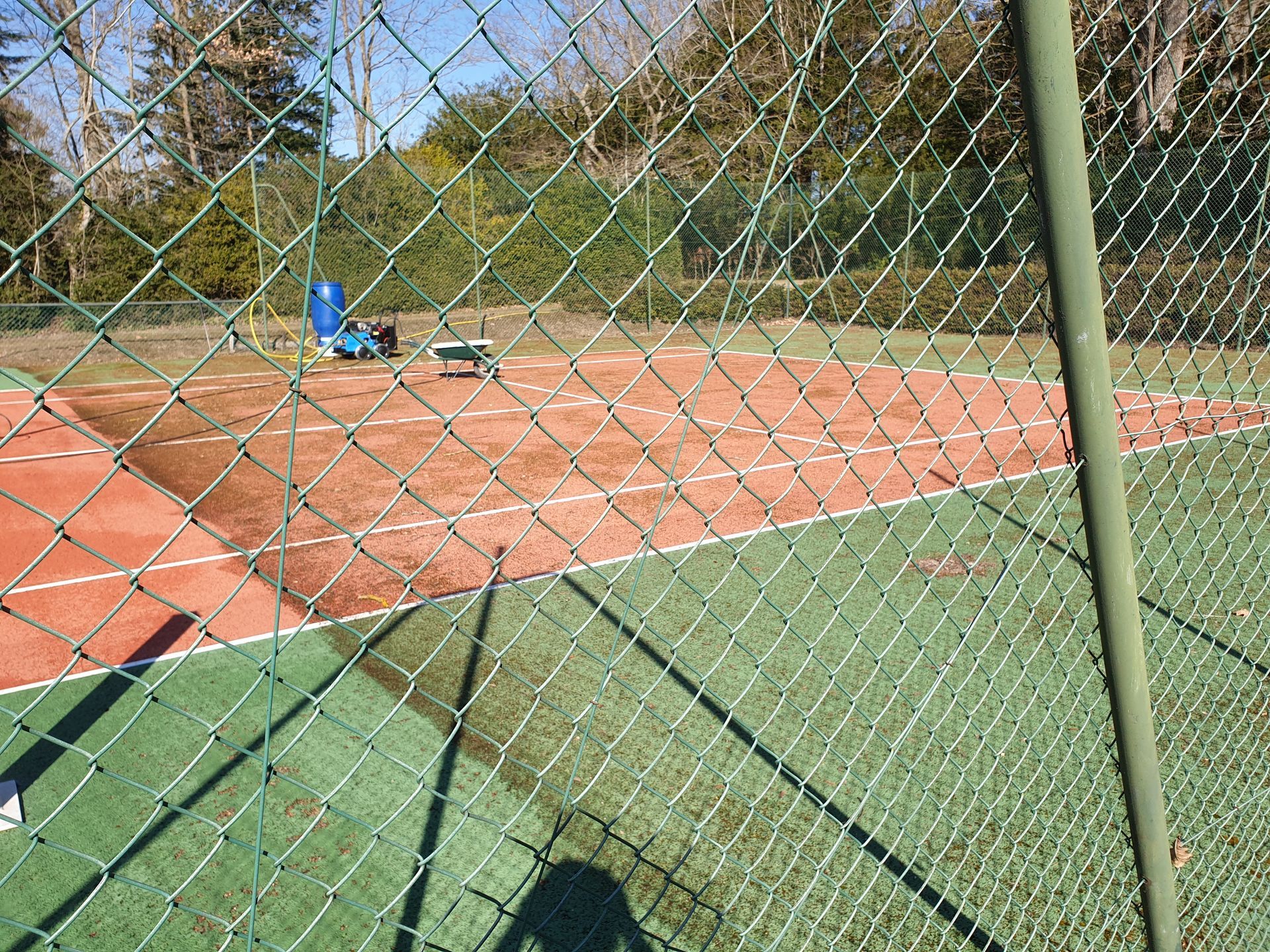 Court de tennis derrière une clôture en grillage vert. Le court possède une surface verte et une aire de jeu brun rougeâtre.
