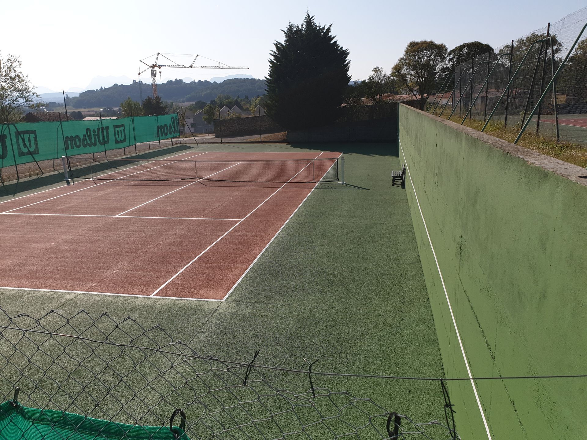 Court de tennis avec surface en terre battue rouge, gazon artificiel vert et mur vert en arrière-plan.