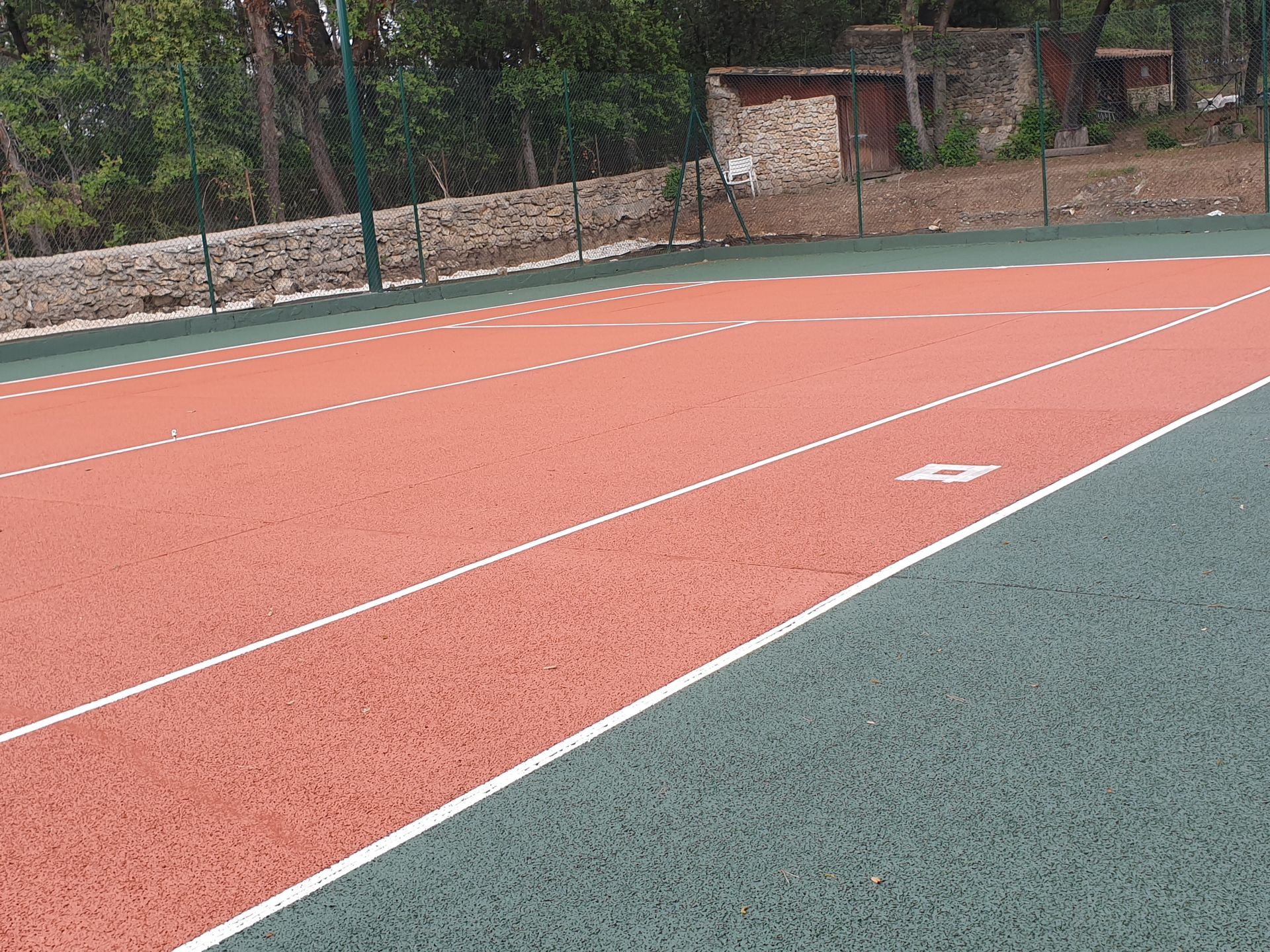 Piste d'athlétisme rouge à couloirs blancs, bordée d'une surface verte. À l'arrière-plan, un mur et des arbres.