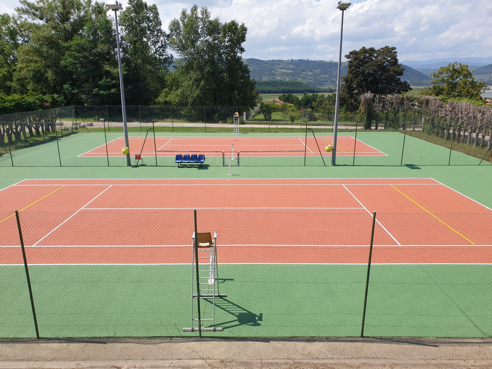 Deux courts de tennis extérieurs, l'un vert et l'autre rouge ; ils sont entourés d'une clôture.