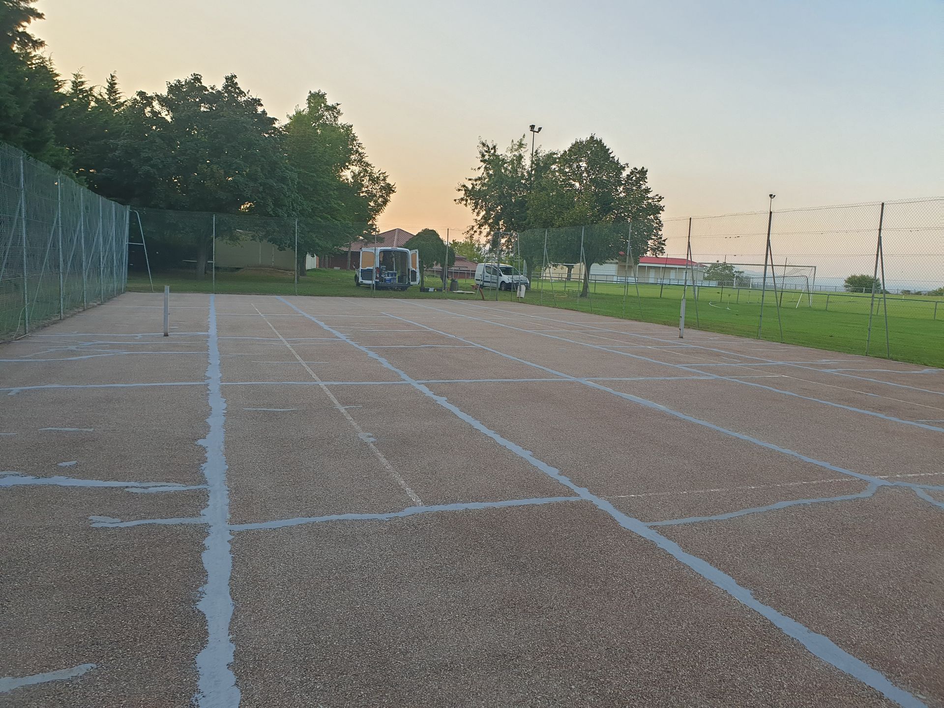 Terrain extérieur aux marquages ​​gris, recouvert d'un matériau marron, sous un ciel crépusculaire.