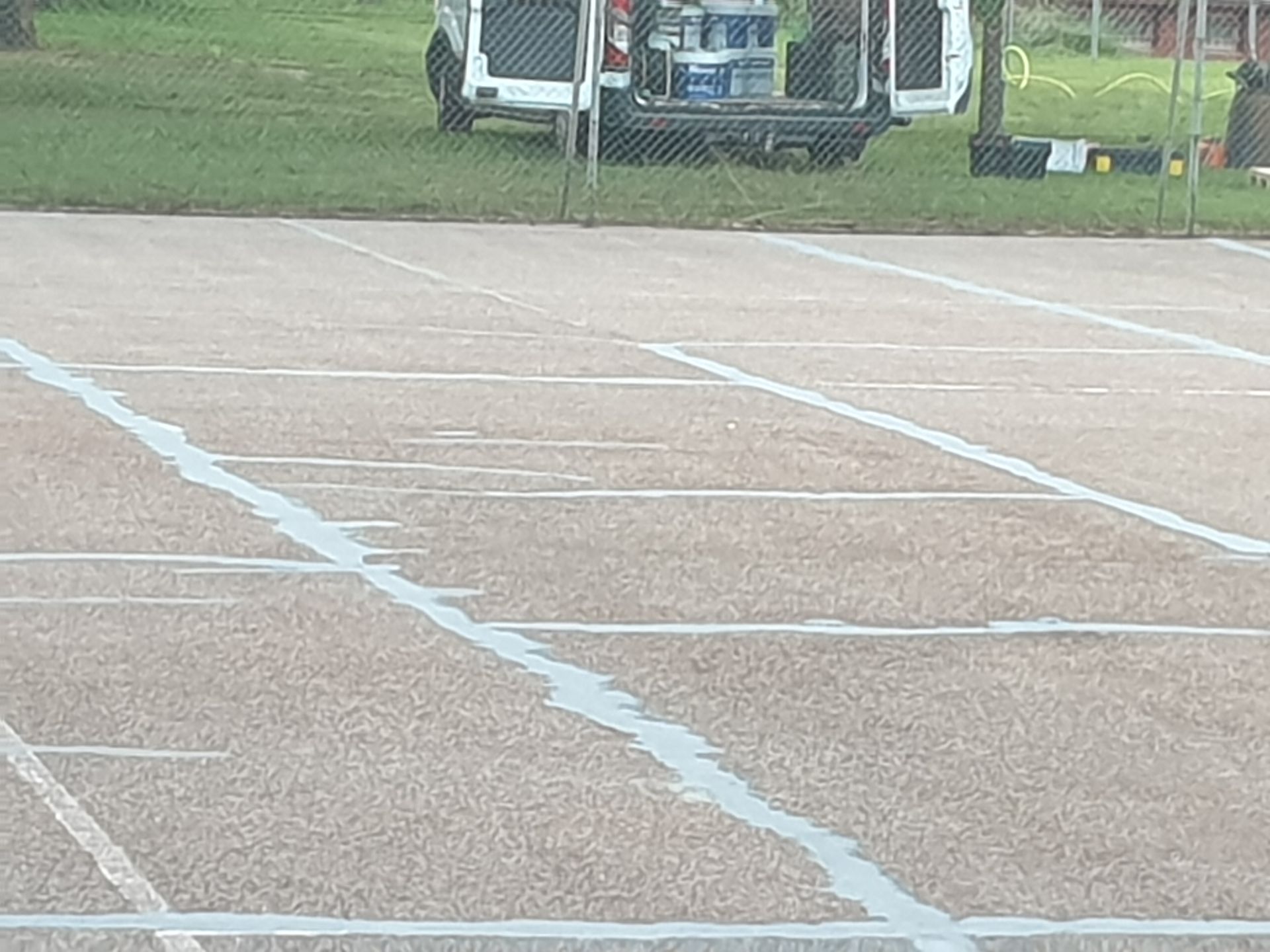 Court de tennis aux lignes blanches fraîchement peintes. Une camionnette est garée derrière le court, près d'une zone herbeuse.
