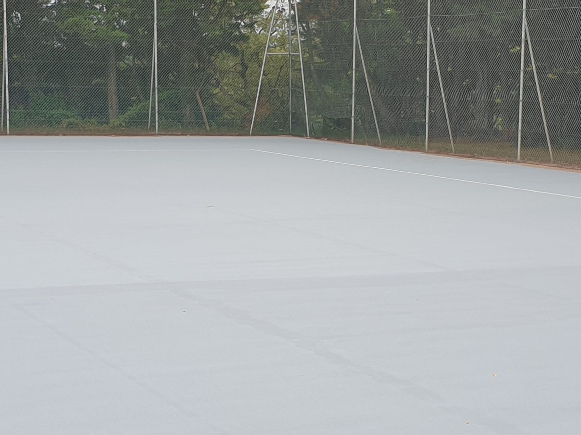 Court de tennis gris avec lignes blanches et clôture en arrière-plan.