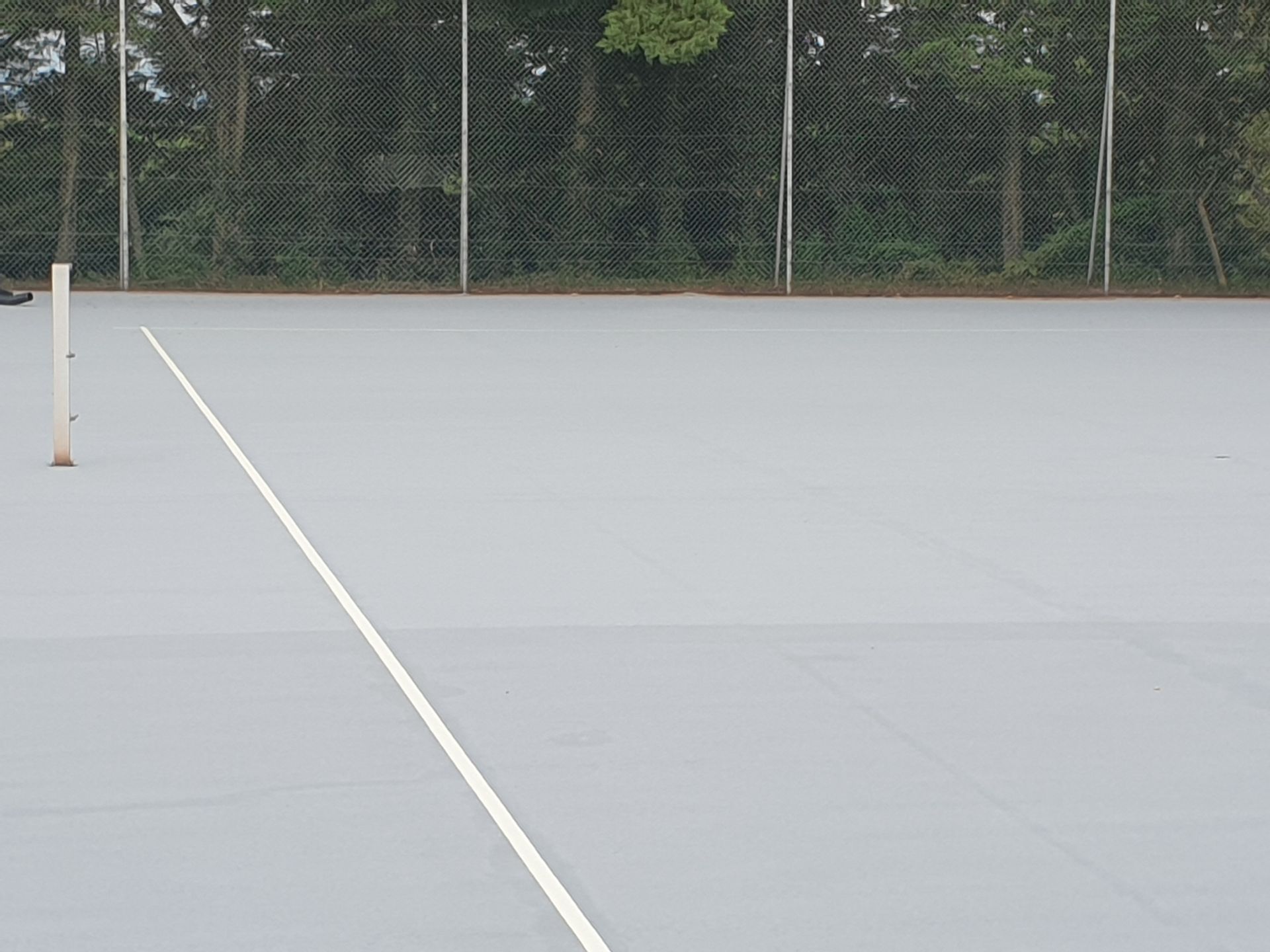 Court de tennis gris vide, avec des lignes blanches et un filet en arrière-plan.