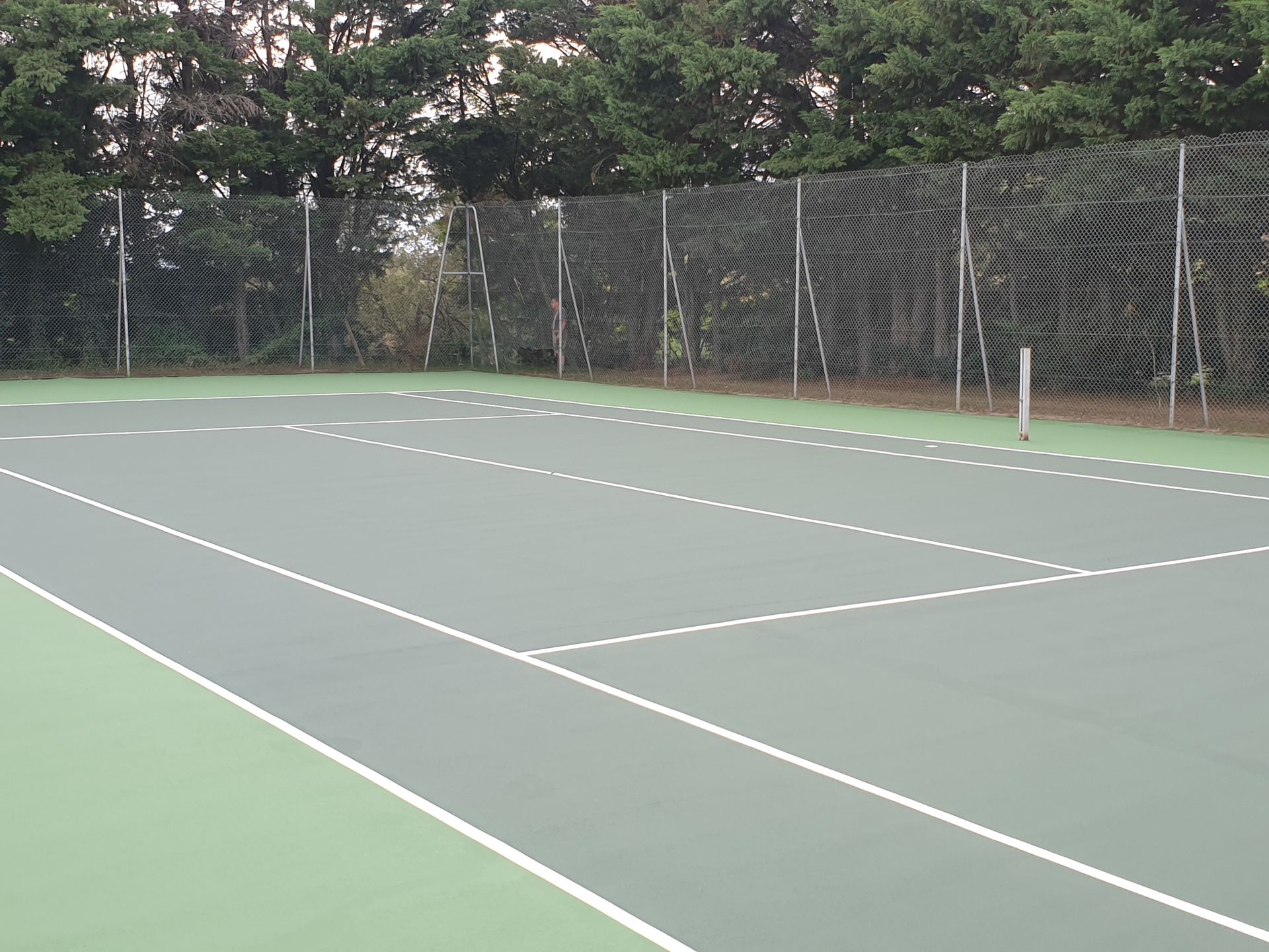 Court de tennis avec surface verte, lignes blanches et clôture.