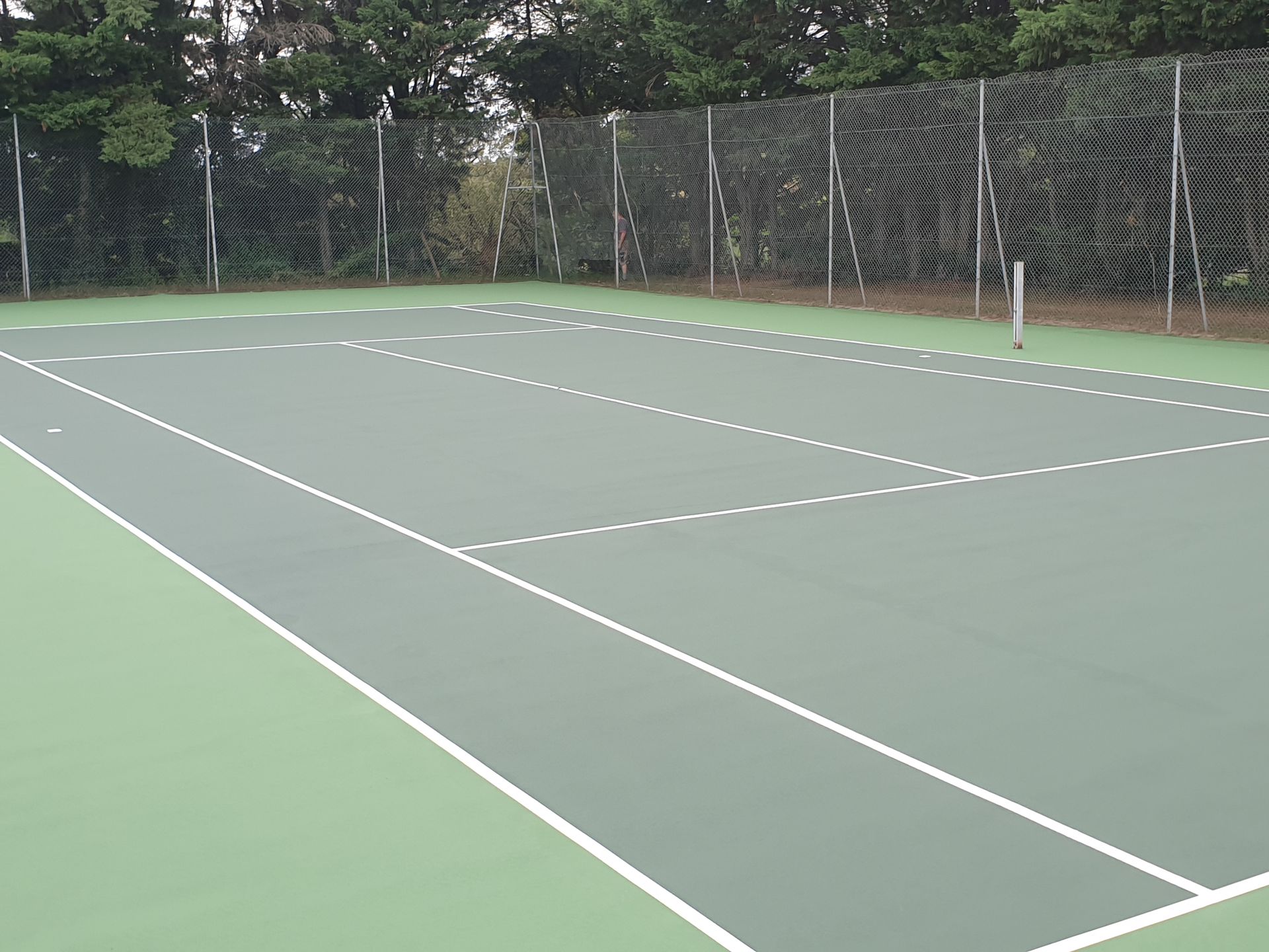 Court de tennis vert vide, avec des lignes blanches et une clôture.