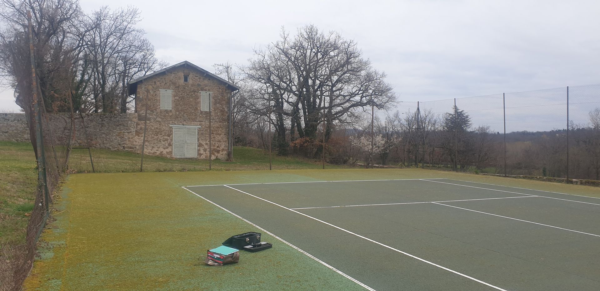 Un terrain de sport extérieur verdoyant avec un petit bâtiment en pierre et des arbres dénudés en arrière-plan.