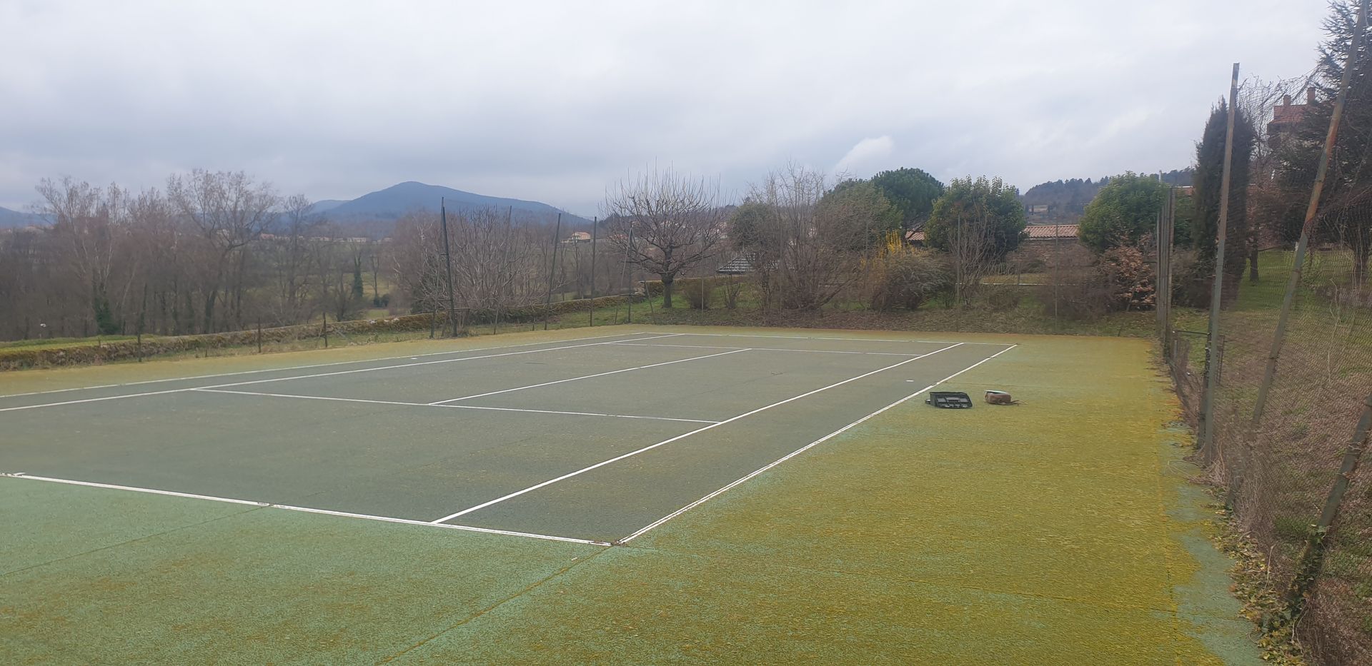 Terrain de sport extérieur avec marquages ​​blancs sur gazon synthétique vert, sous un ciel nuageux.