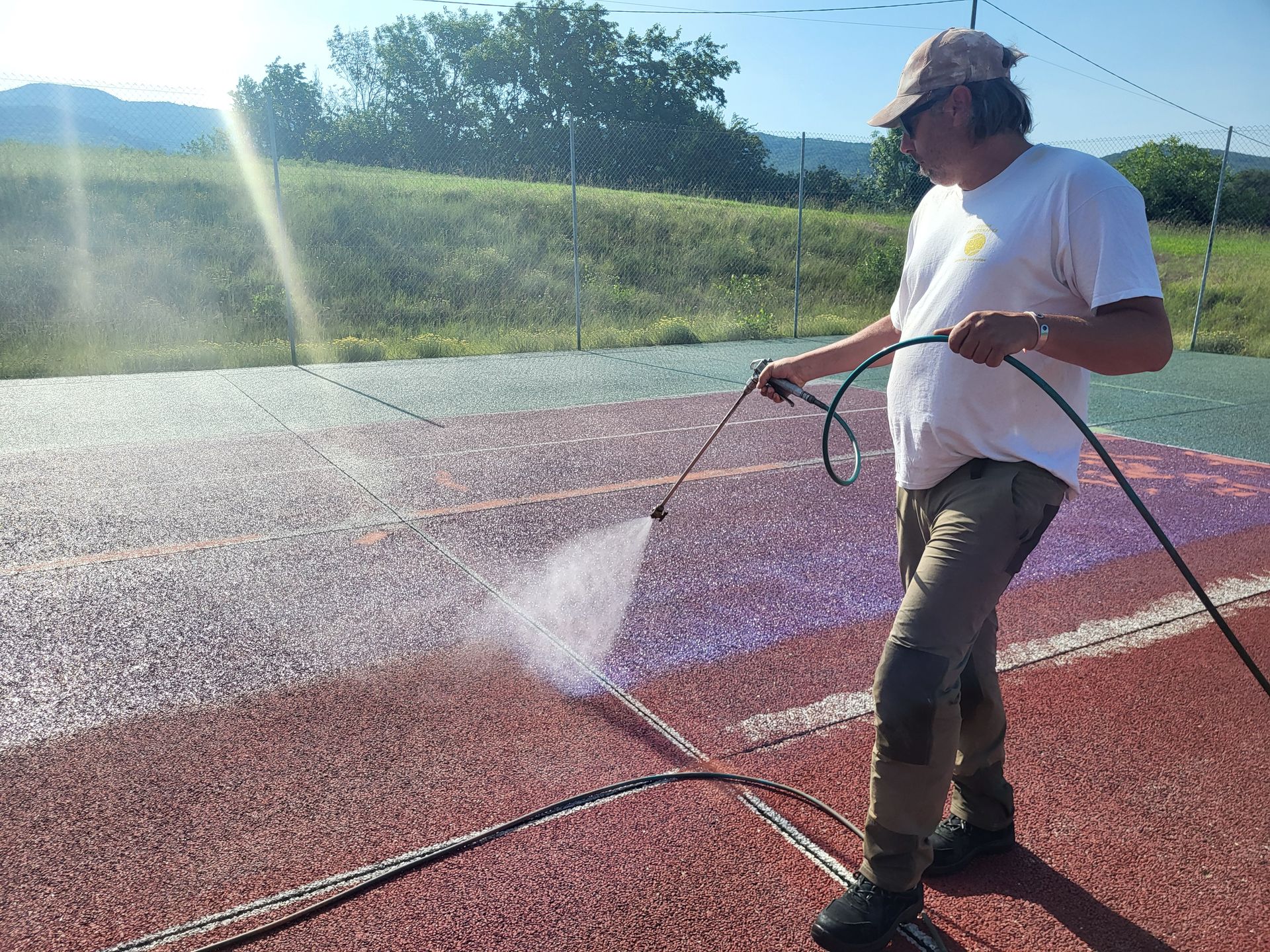 Un homme asperge d'eau un court de tennis, en extérieur.