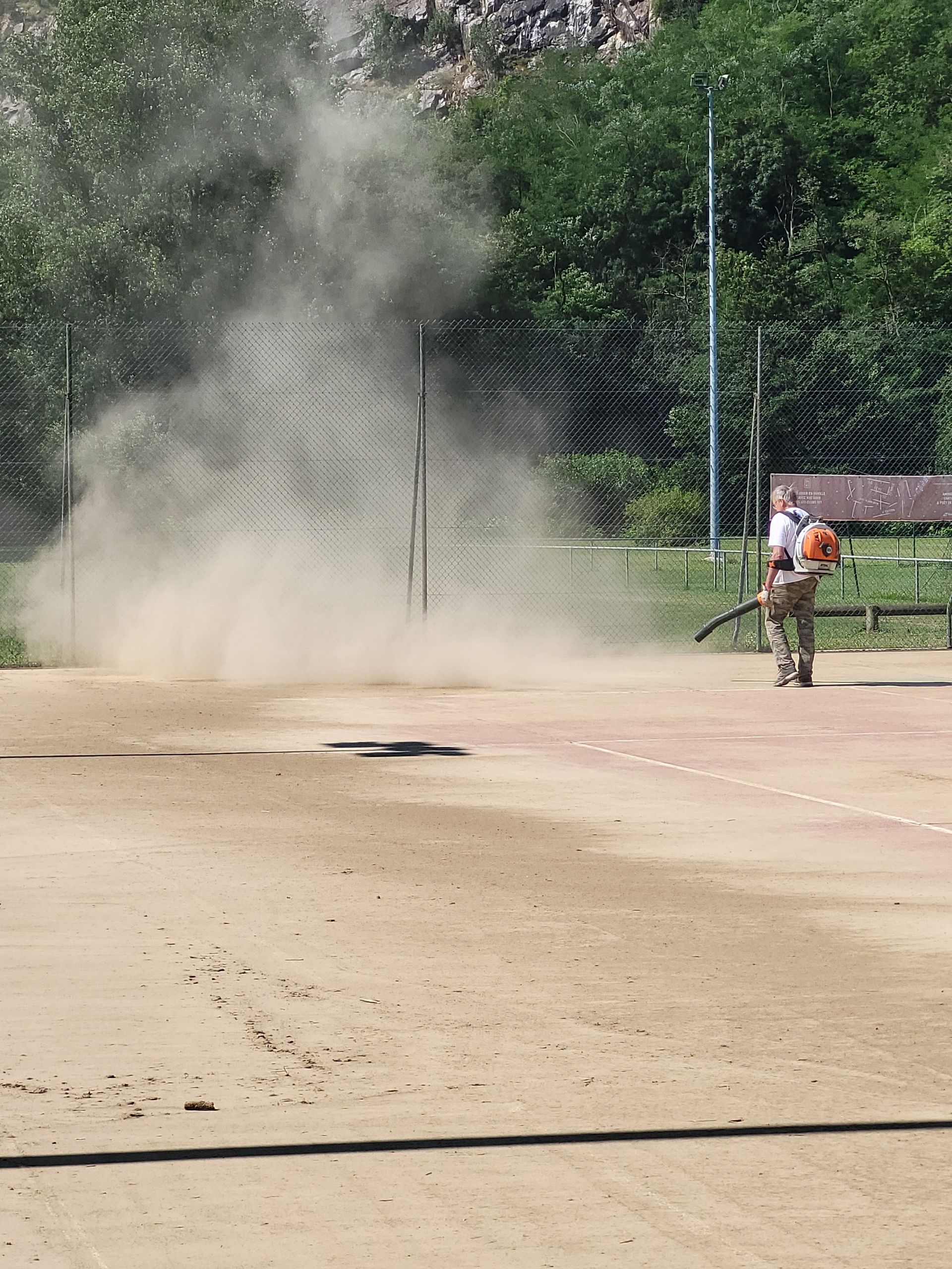 Personne utilisant un souffleur de feuilles sur une surface extérieure poussiéreuse.