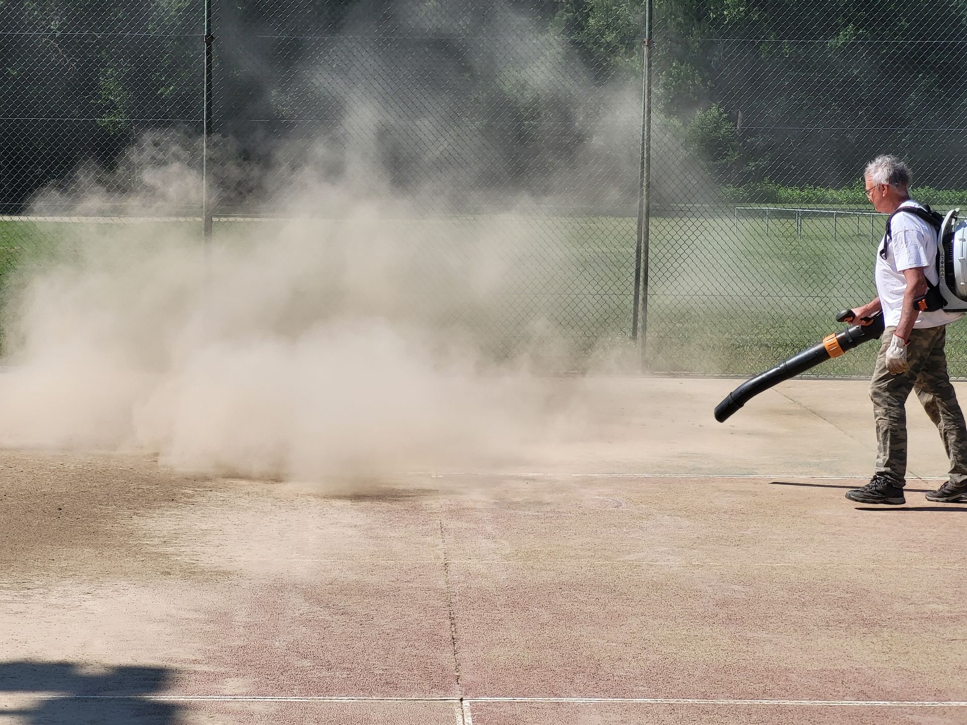 Un homme souffle la poussière d'un terrain de base-ball à l'aide d'un souffleur à feuilles.