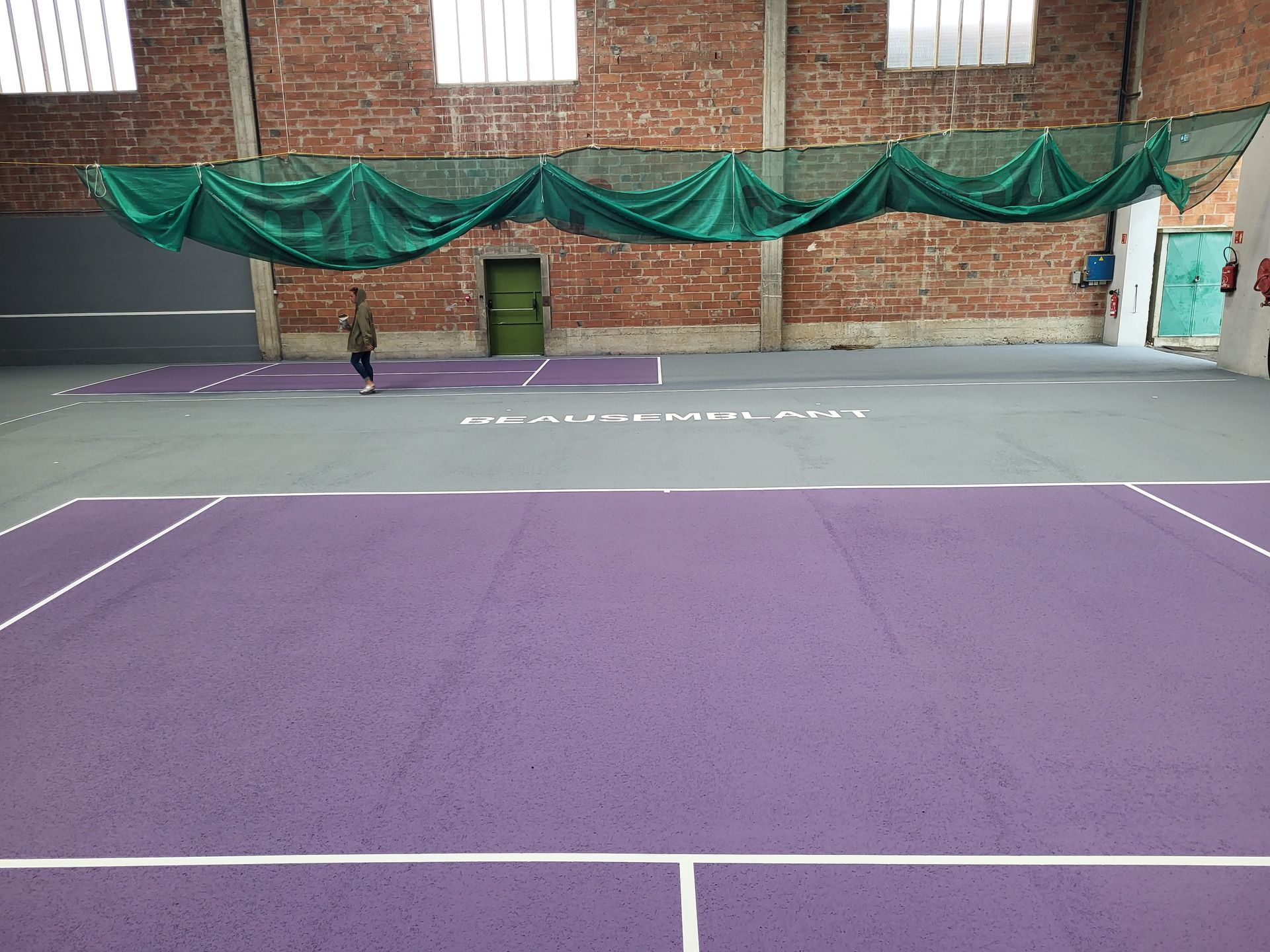Court de tennis intérieur avec surface de jeu violette, lignes blanches et une personne debout près du centre.