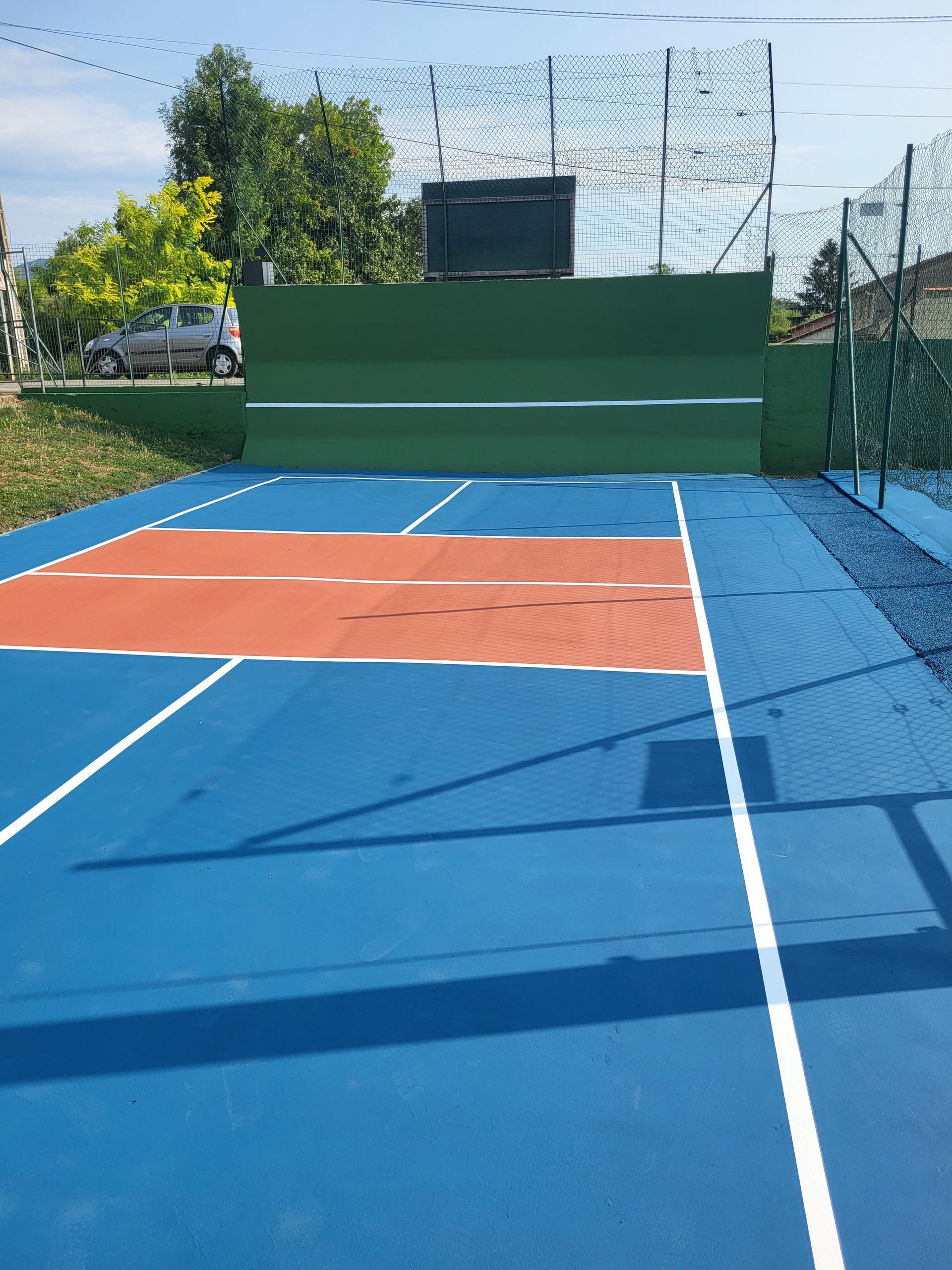 Terrain de sport extérieur bleu et orange avec mur vert, filet et ciel bleu.