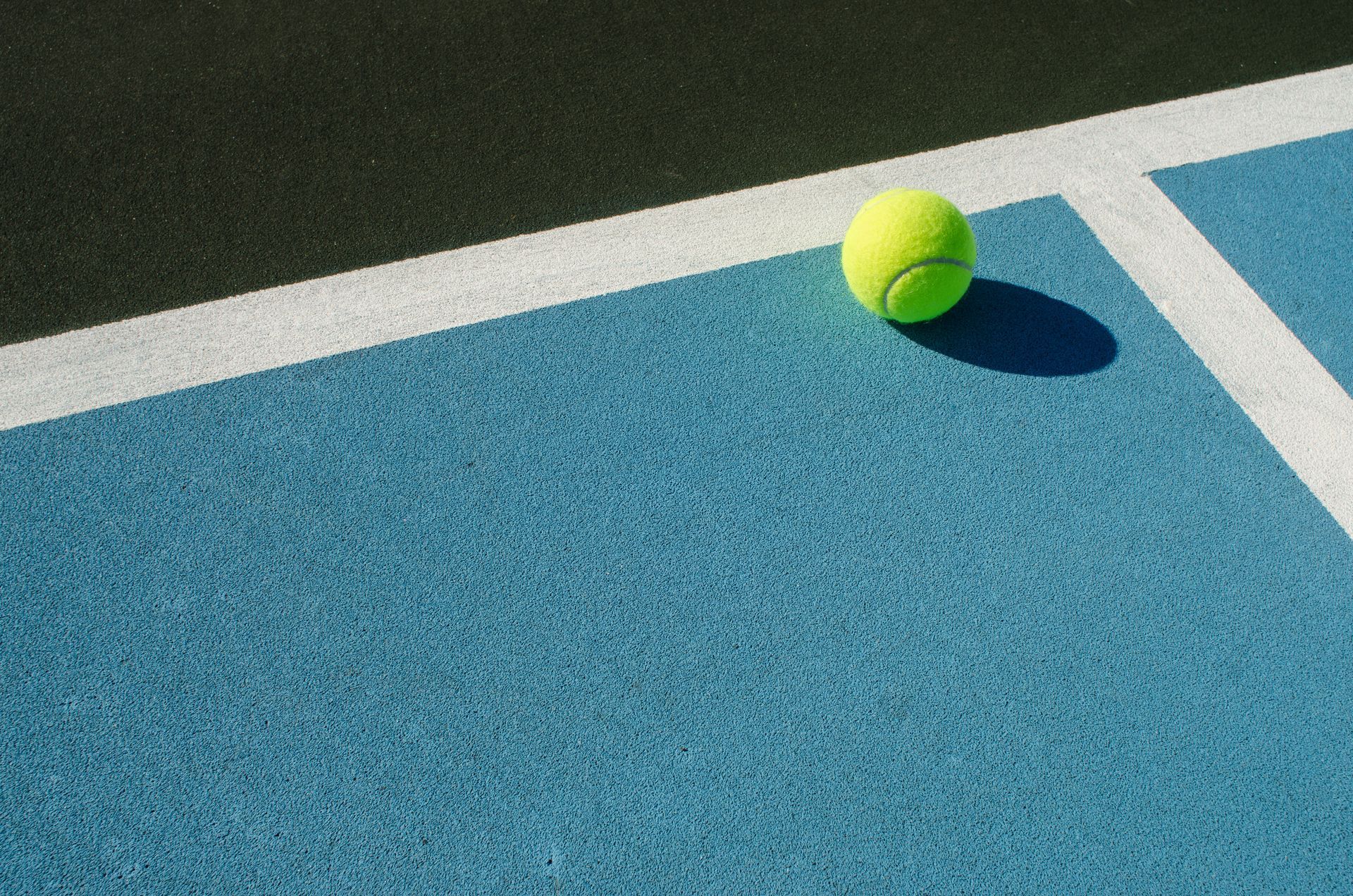 Balle de tennis sur un court de tennis bleu et noir avec des lignes blanches.