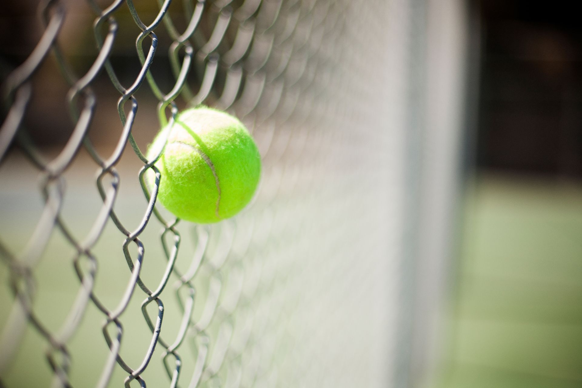 Balle de tennis jaune coincée dans un grillage, à l'extérieur, sur un court de tennis.