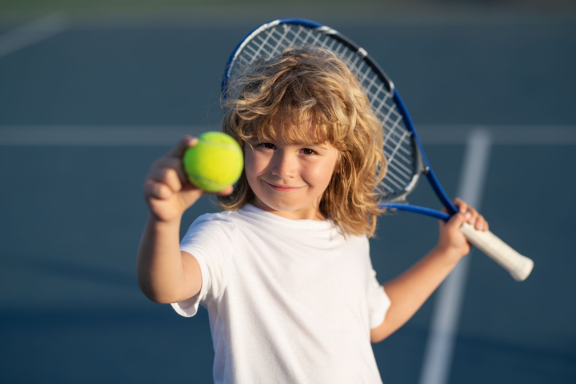 Garçon souriant avec une raquette et une balle de tennis sur un court de tennis.