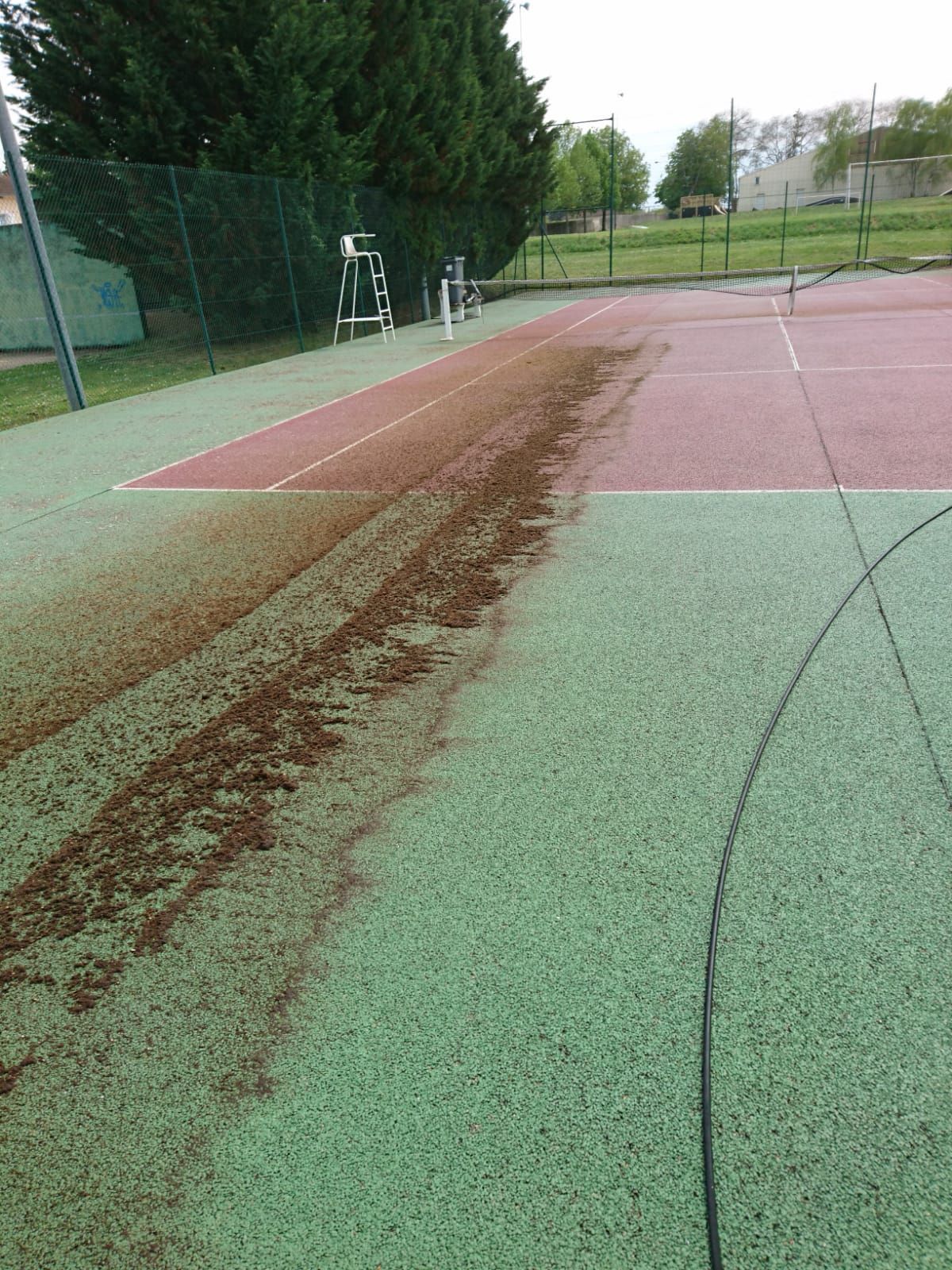 Court de tennis avec des débris bruns éparpillés sur des surfaces vertes et rouges.