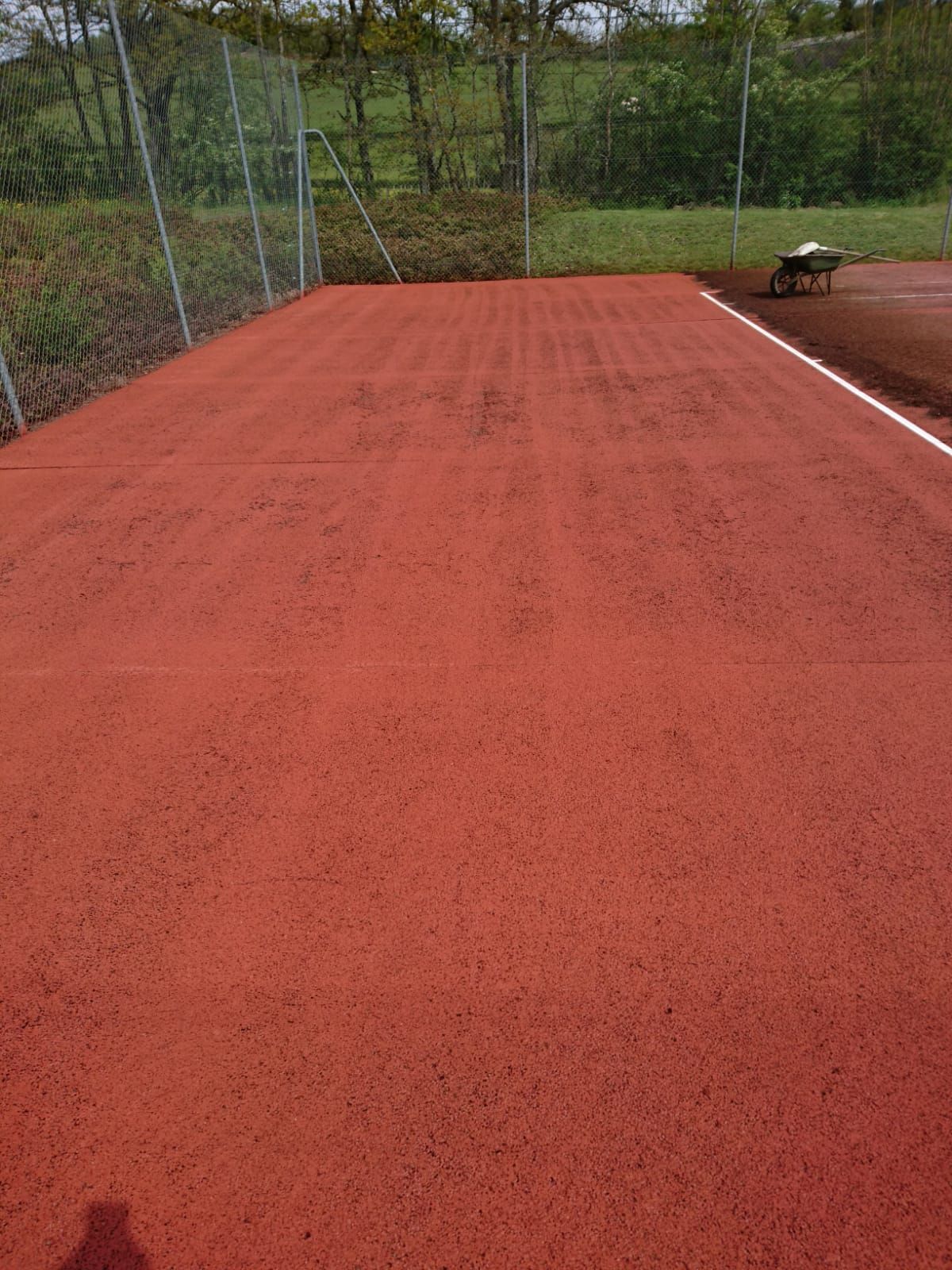 Court de tennis en terre battue rouge avec filet et chariot à roulettes en arrière-plan.